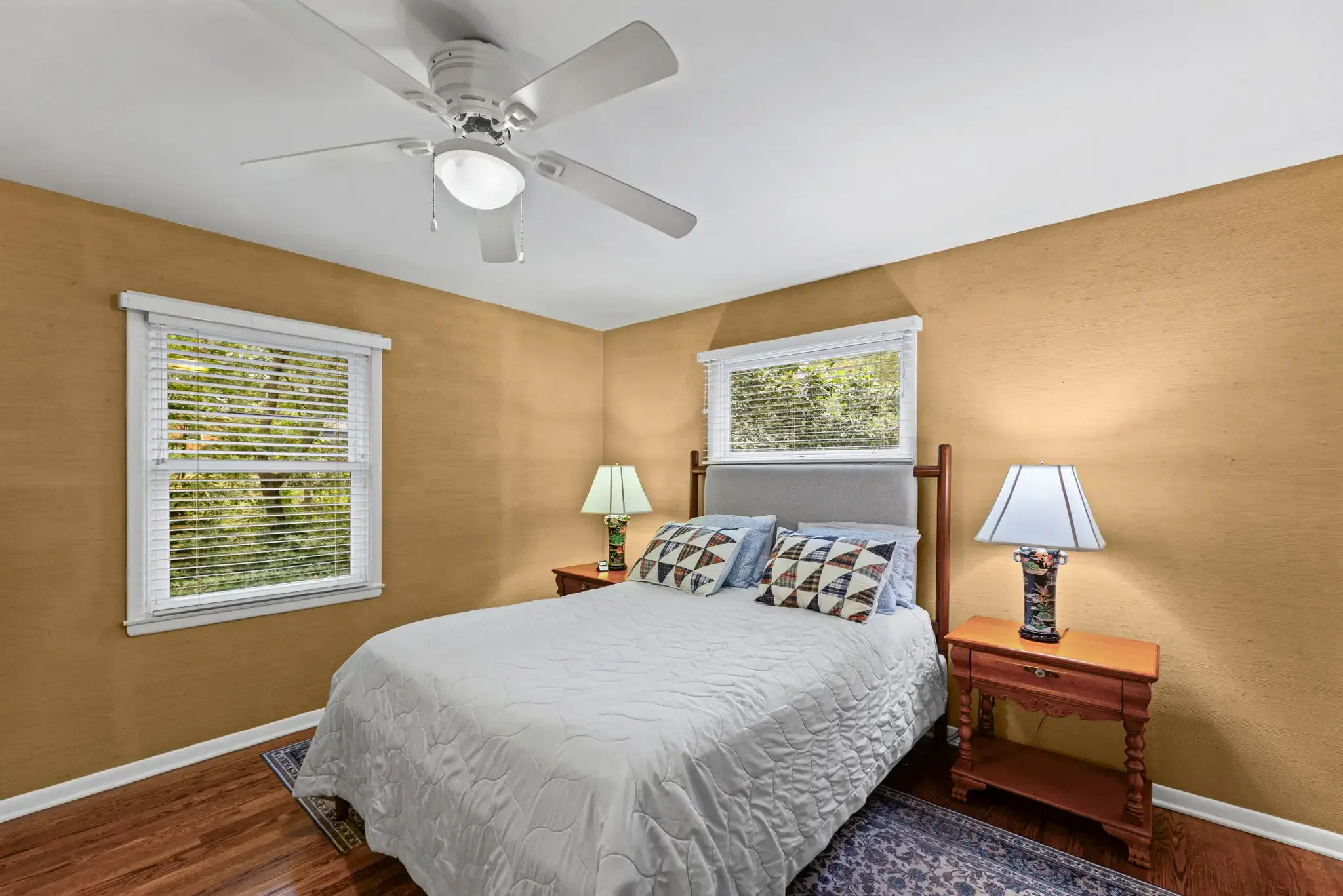 Primary bedroom with hardwood floors and windows on two walls