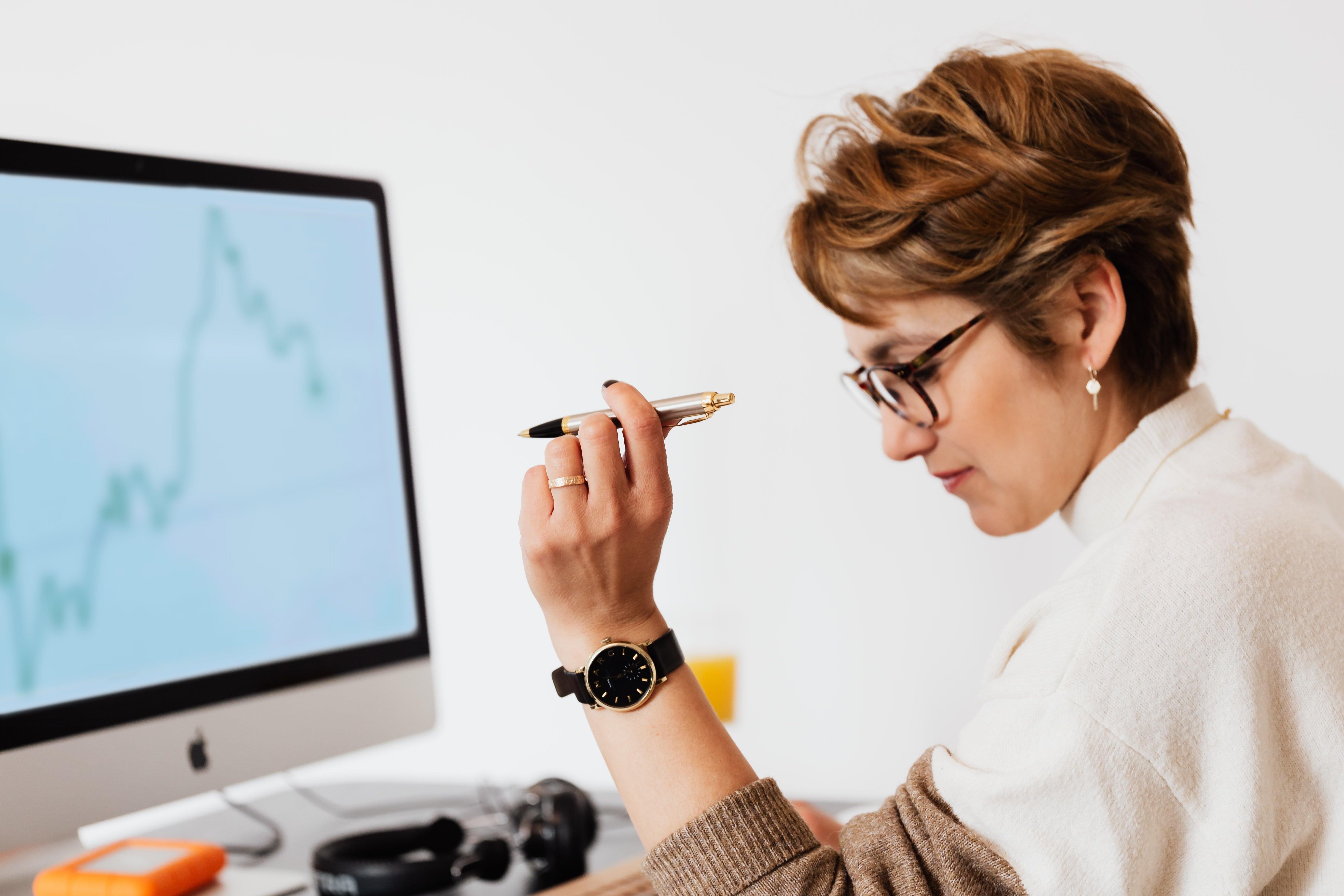 A woman studying a trend line in front of a computer with a pen in her hand