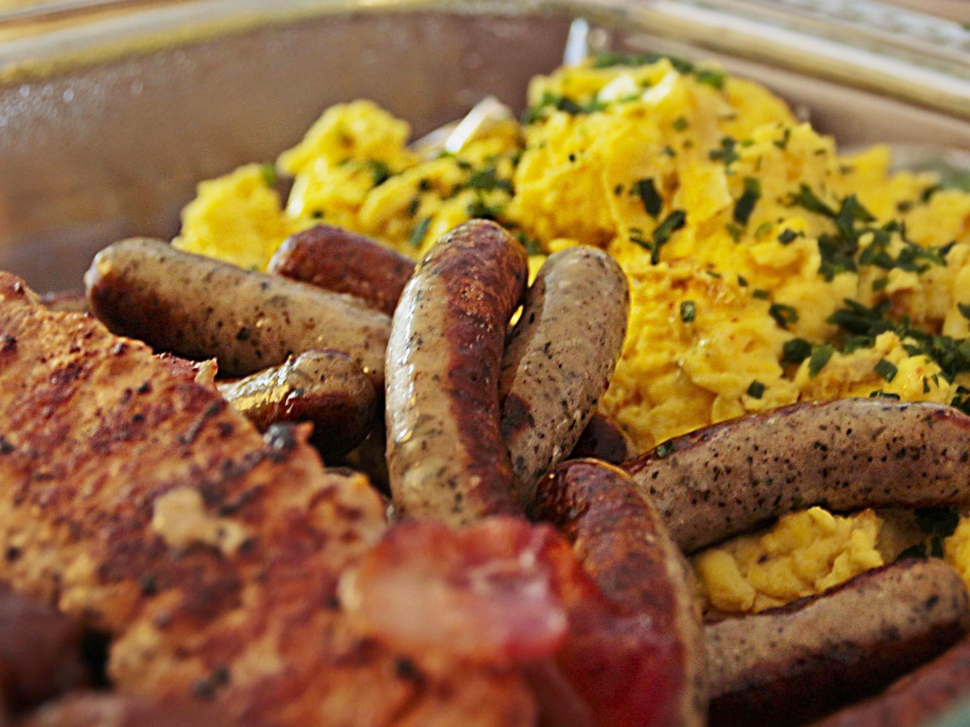 A plate of breakfast food including sausage, scrambled eggs, hashbrowns, and bacon