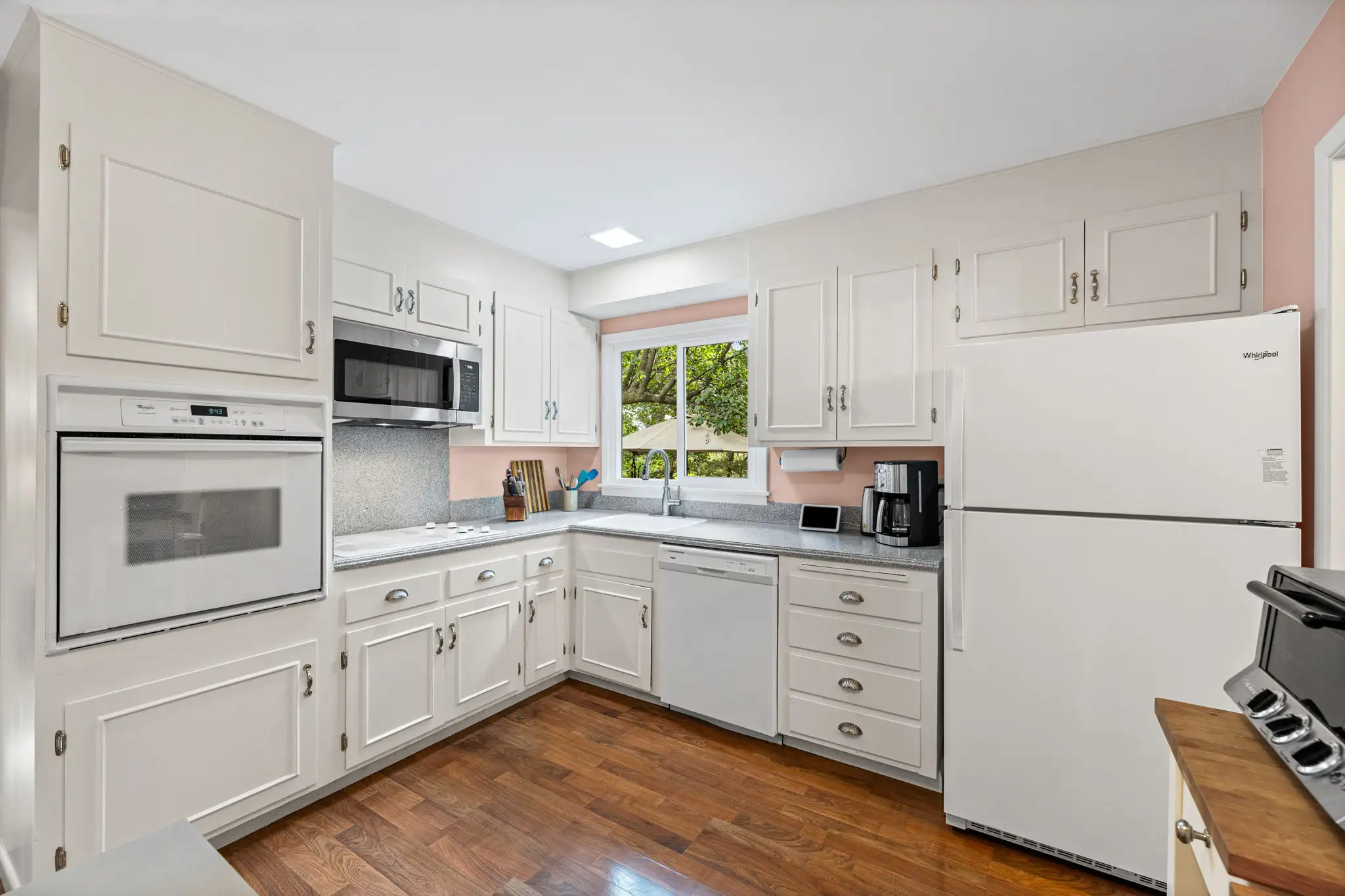 L-shaped kitchen with white cabinetry, a wall oven and a window over the sink