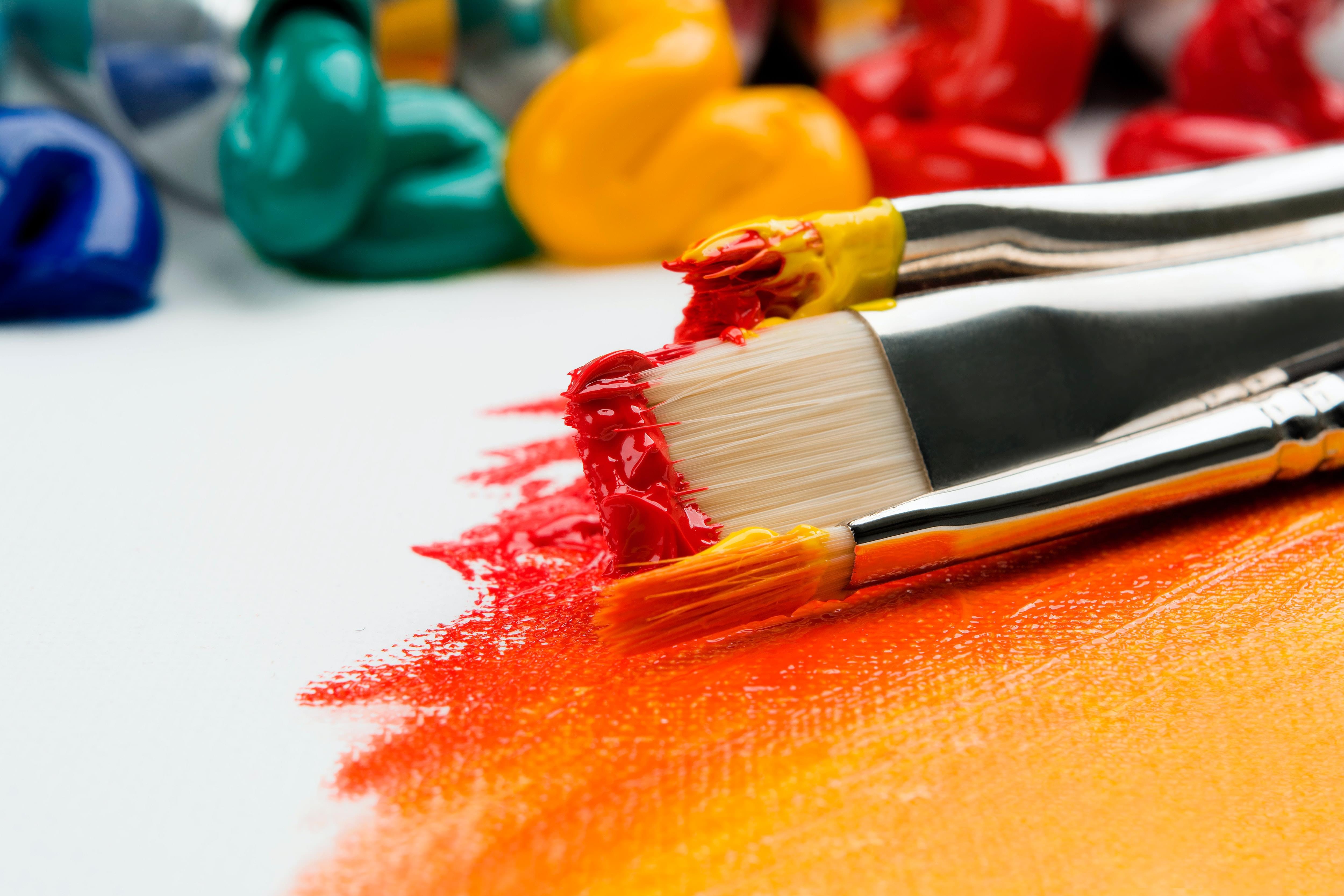 Paintbrushes and red, yellow, and orange paint in the foreground, green and blue paint in the background