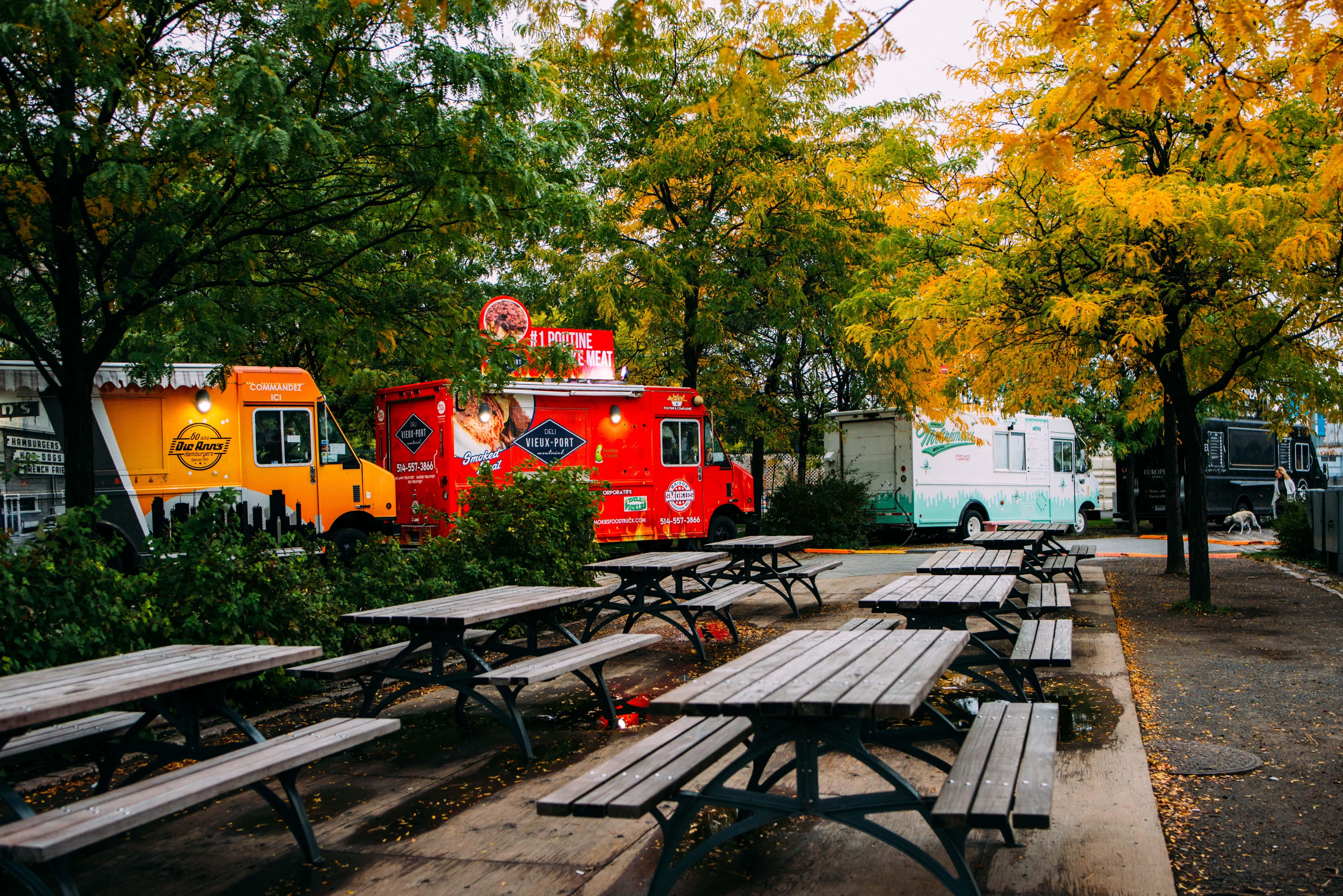 A park filled with picnic tables, leafy trees, and food trucks