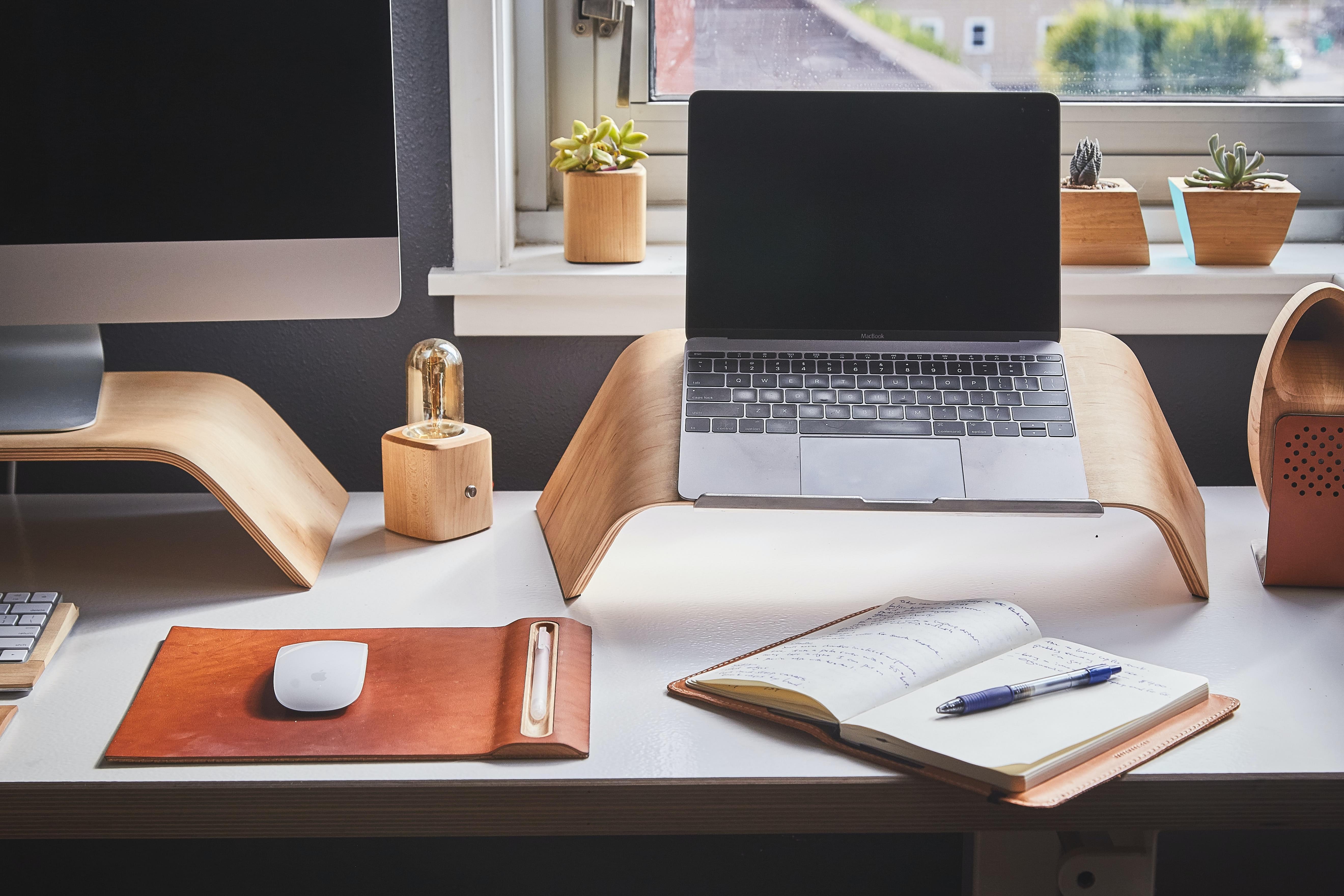 A home office with laptop, monitor, notebook, mouse, and succulents