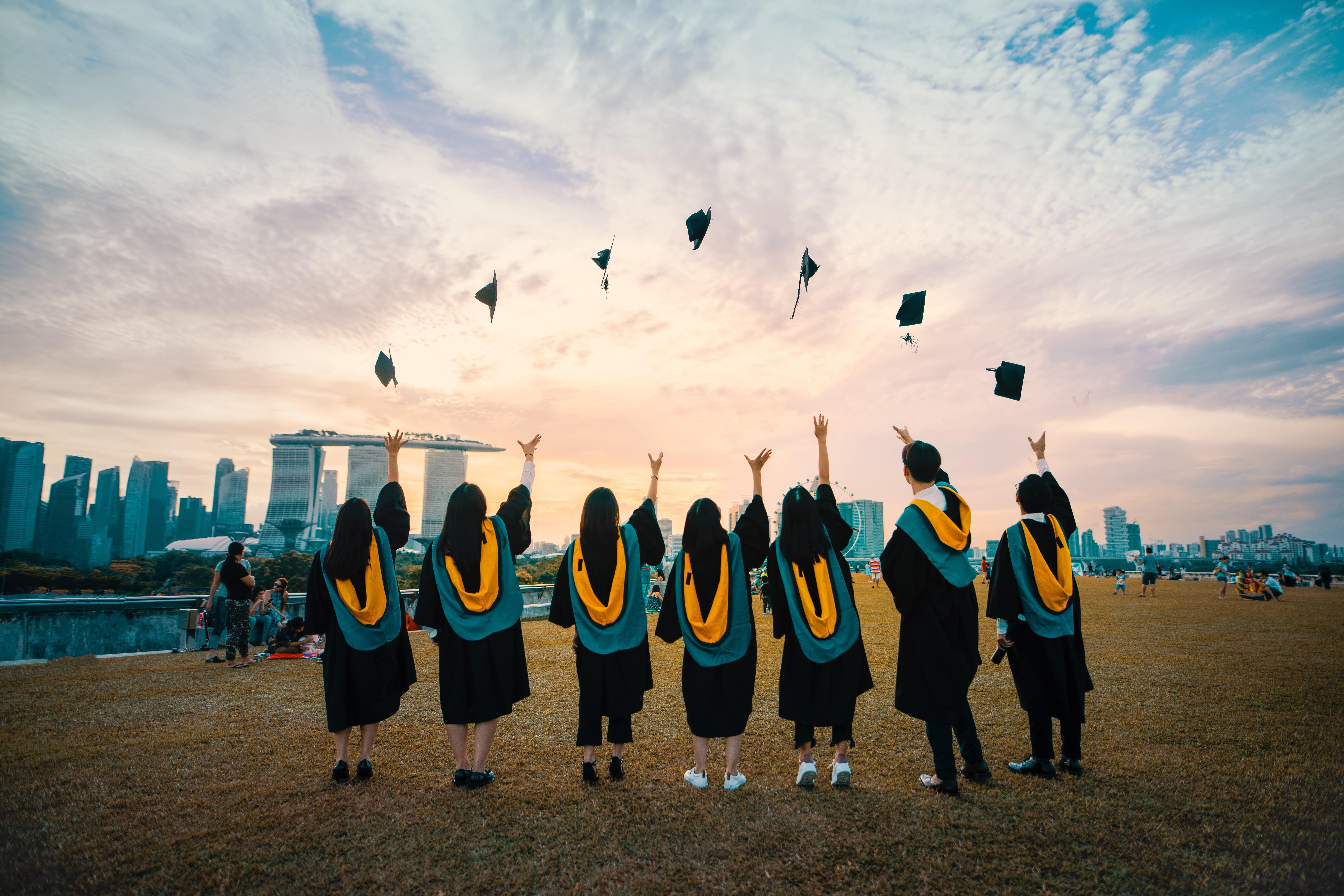 Recent graduates throwing their caps into the air in front of a city backdrop