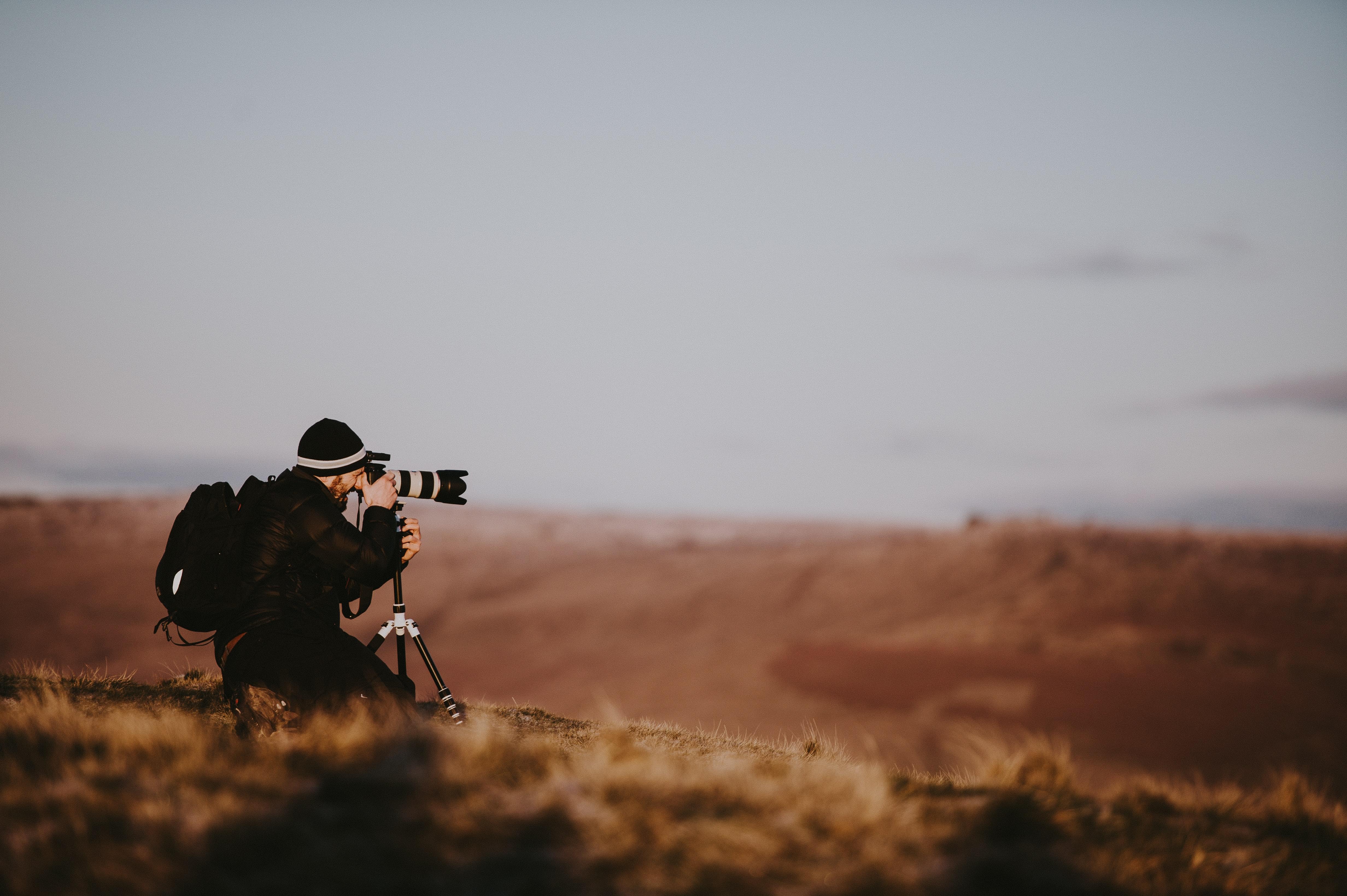 A photographer kneeling behind a camera over a brown landscape