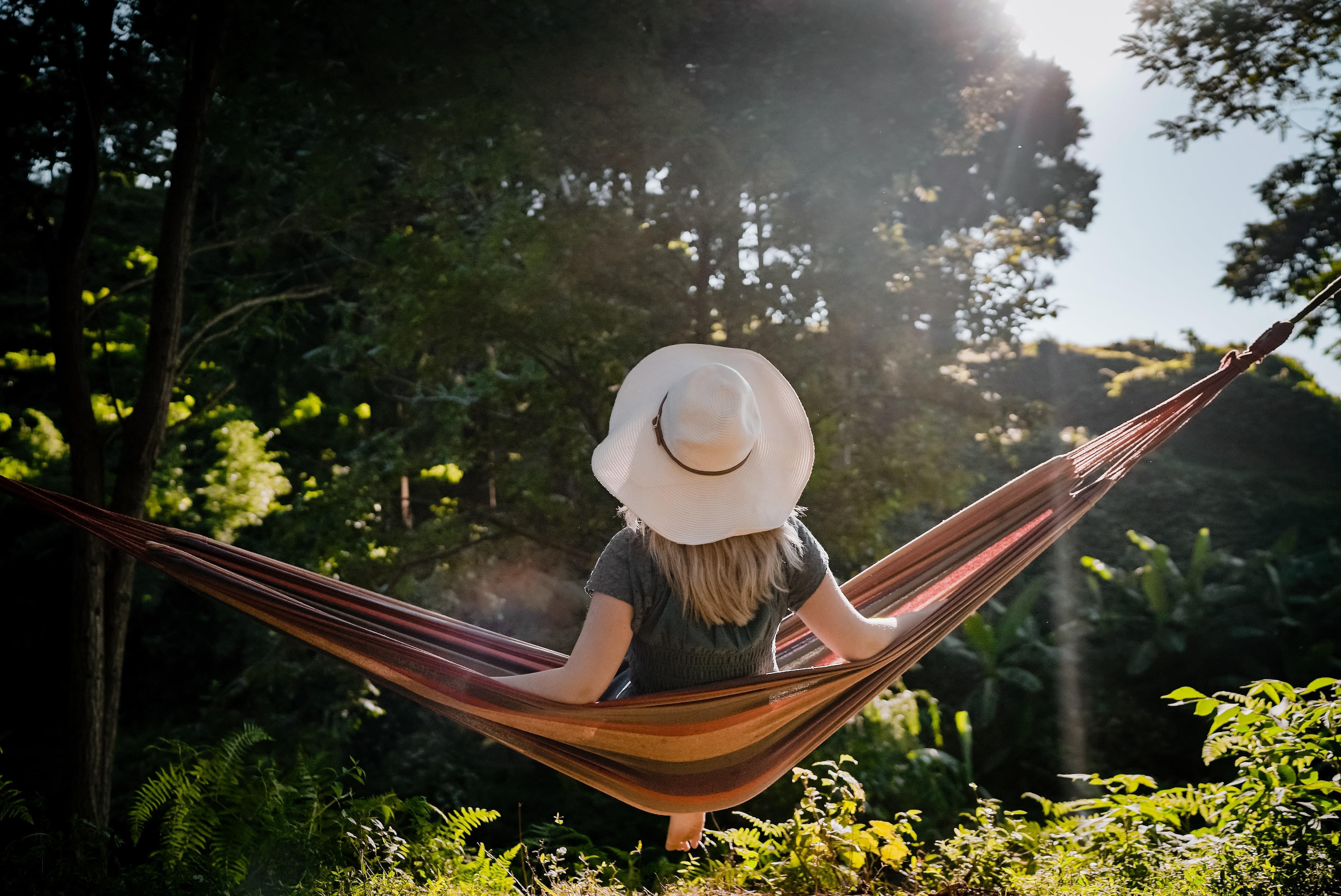 A woman wearing a white hat sitting in a hammock in a green park