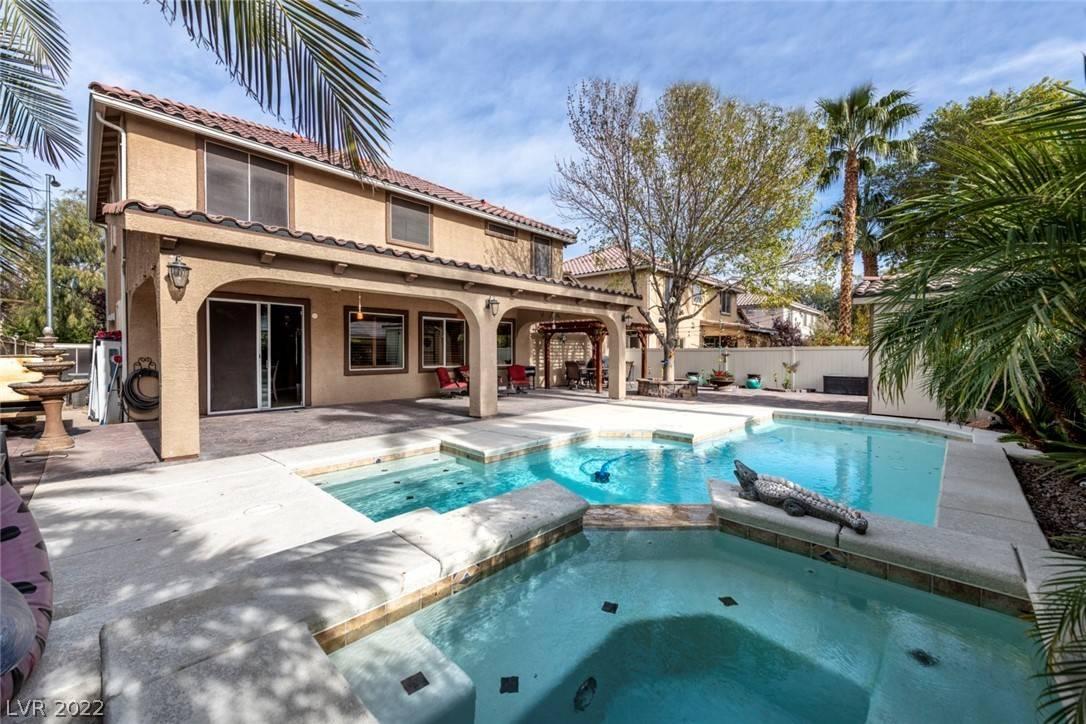 A spacious outdoor area featuring a large pool and large spa, covered patio, and mature trees.