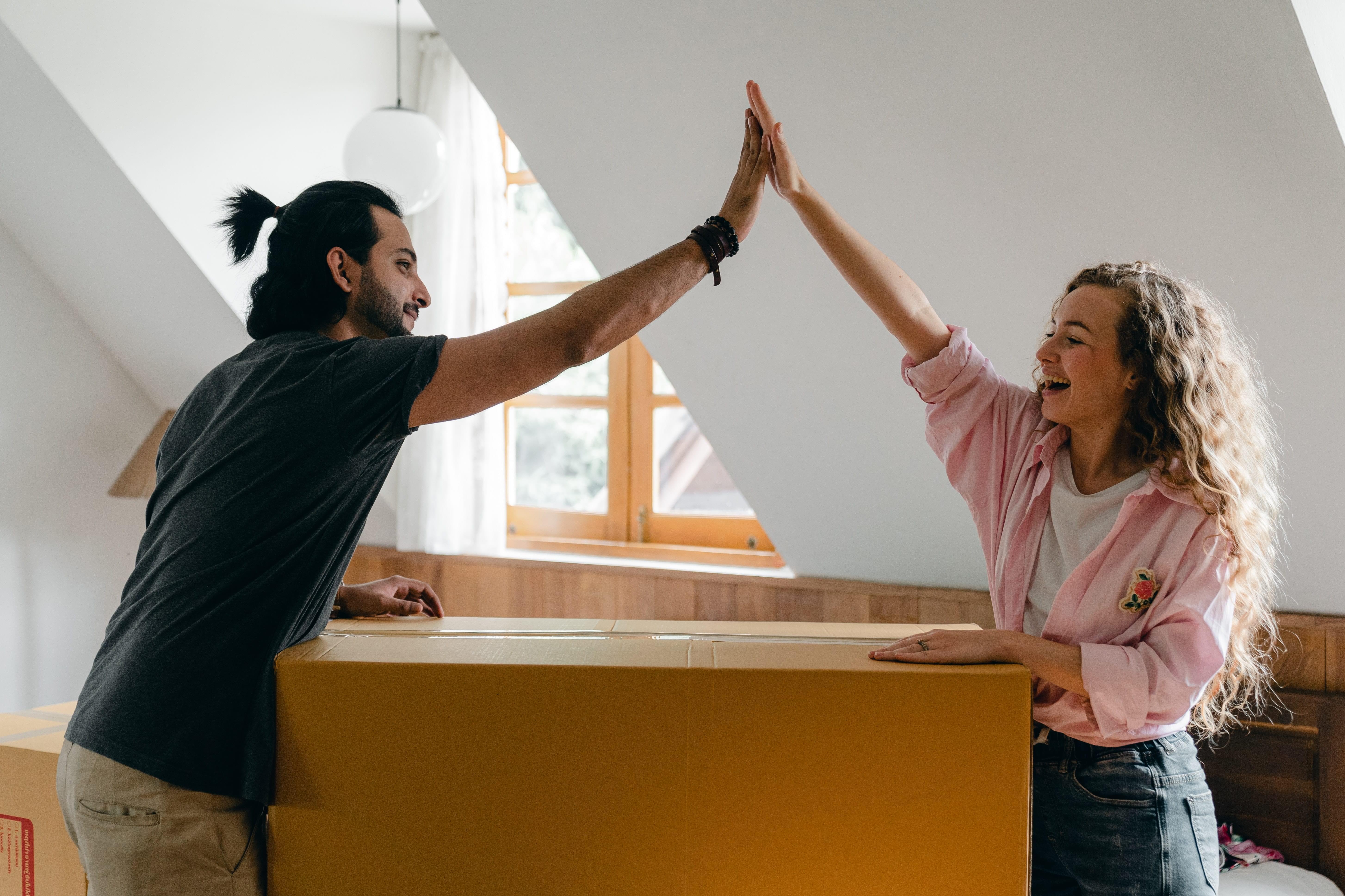 A man and woman high-fiving over a large box moving into their new home