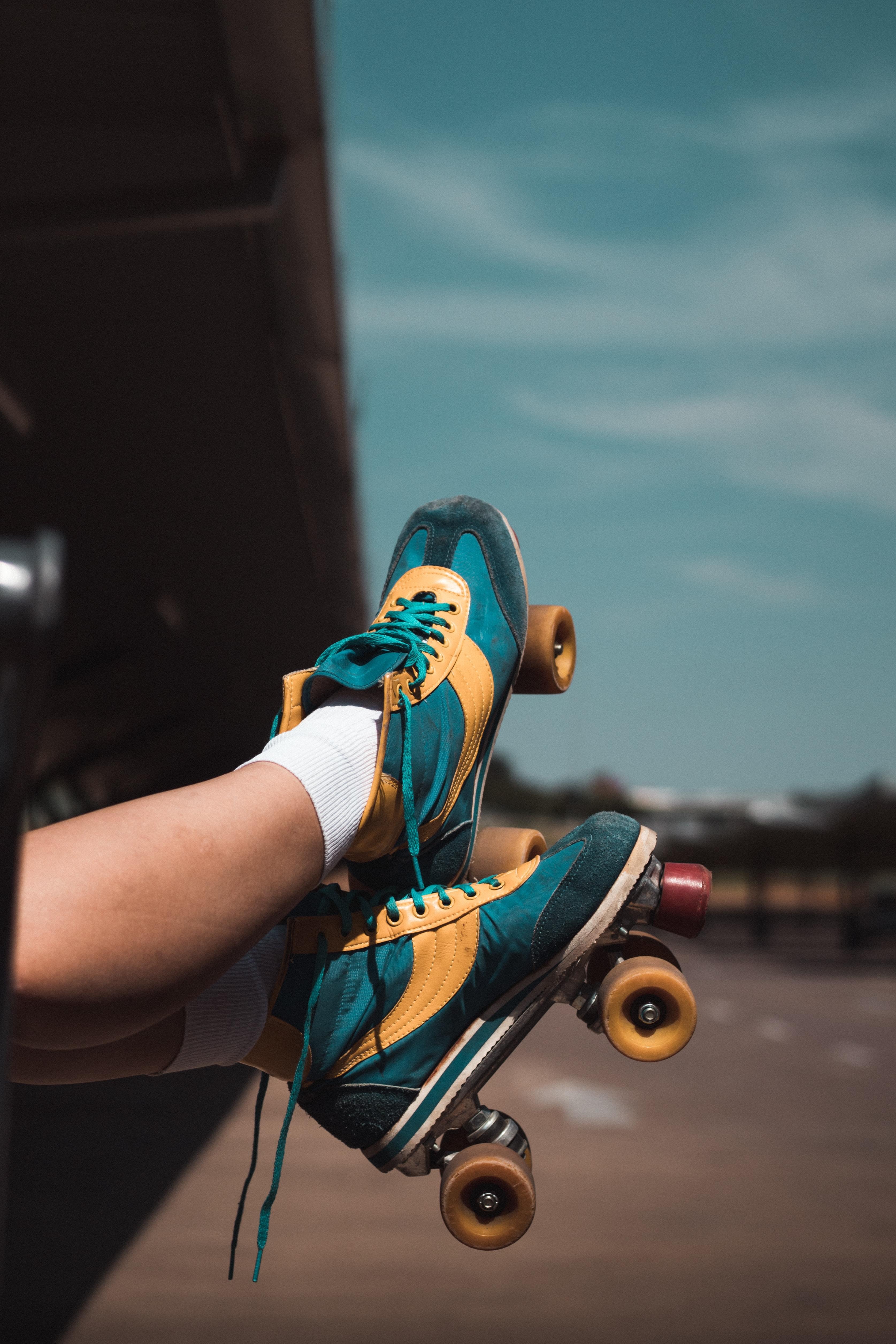 A pair of legs and feet wearing teal roller skates against a blue sky