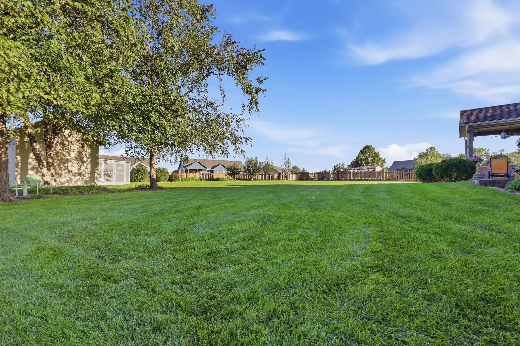 Wide backyard lawn with cedar picket fence and mature trees