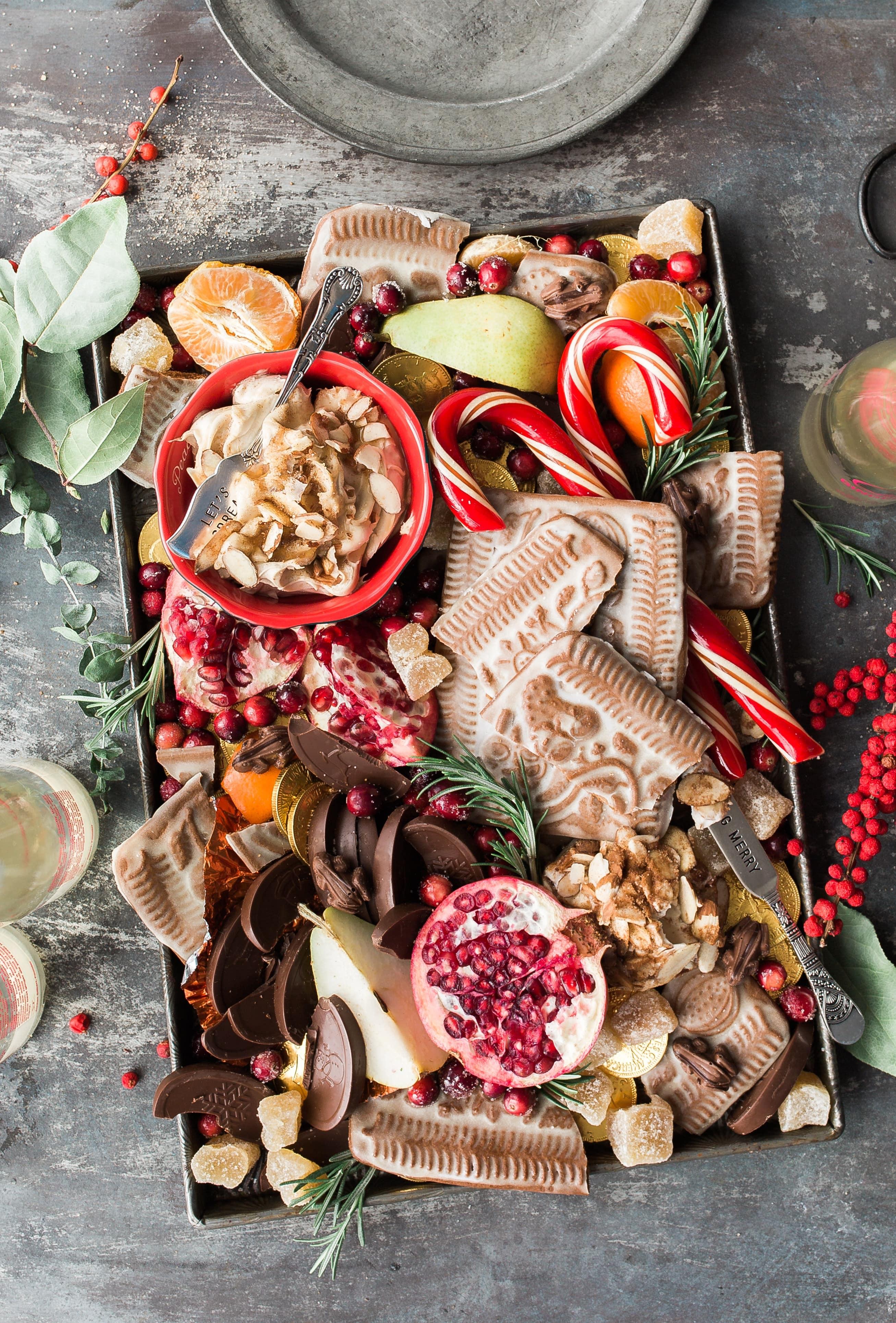 A tray of holiday treats including cookies, fruit, candies, and fresh herbs
