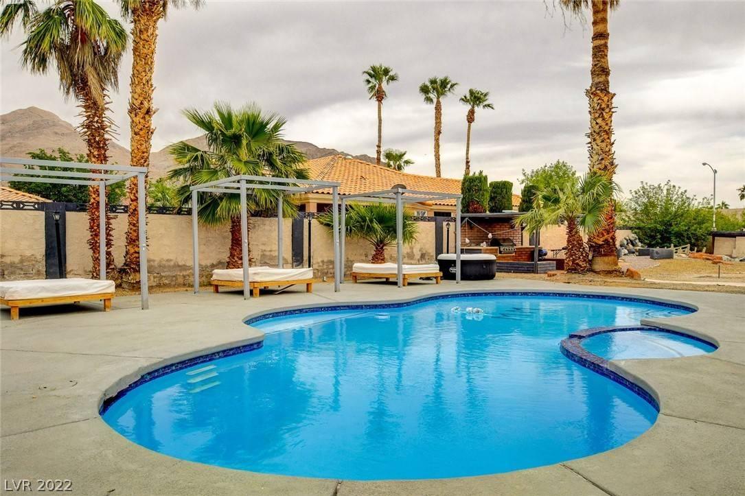 A luxury, resort-like outdoor space featuring a pool spa combination, seating, and huge palms.