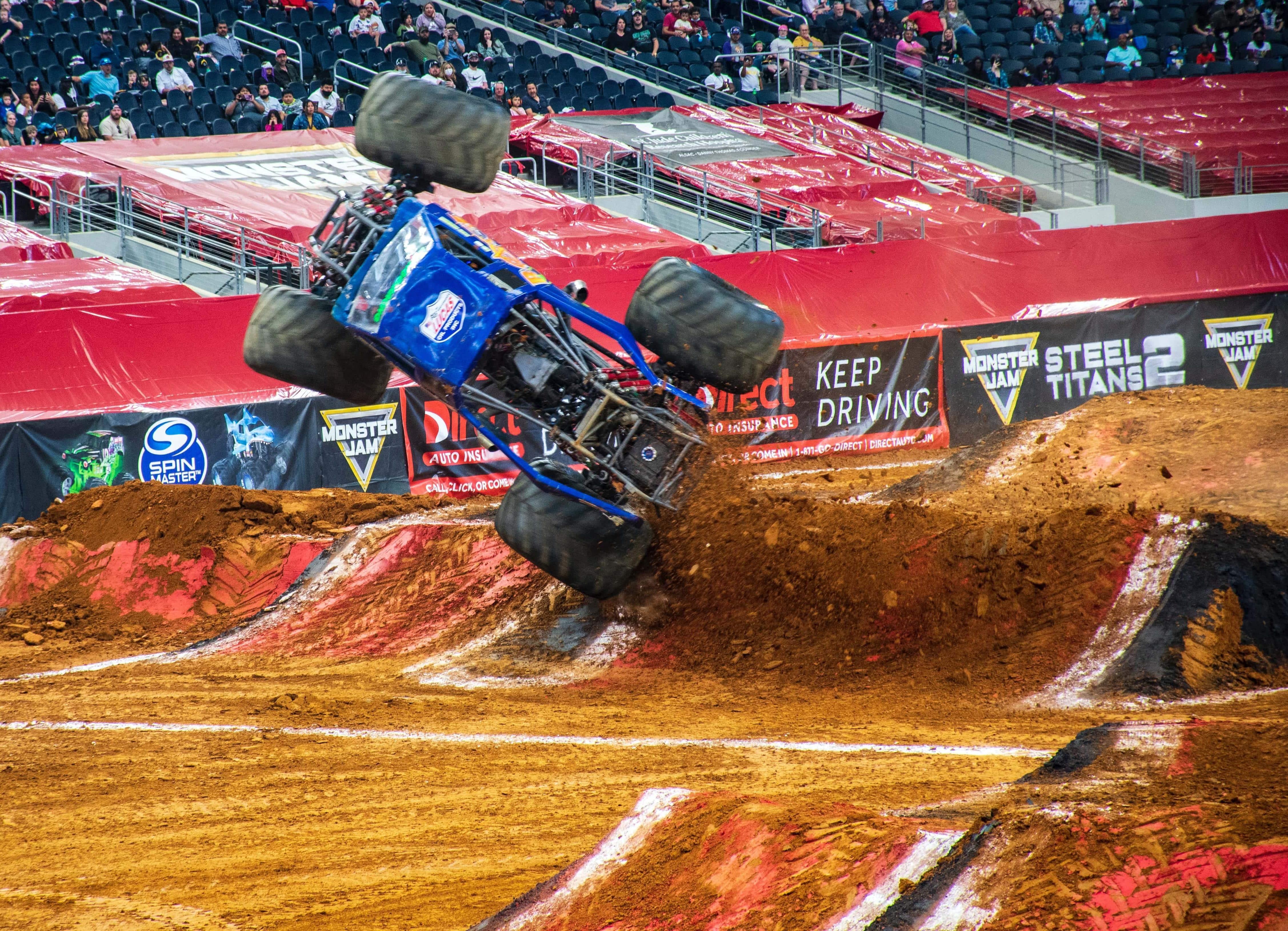 A blue monster truck nearly verticle with three wheels off the ground in the middle of a stunt