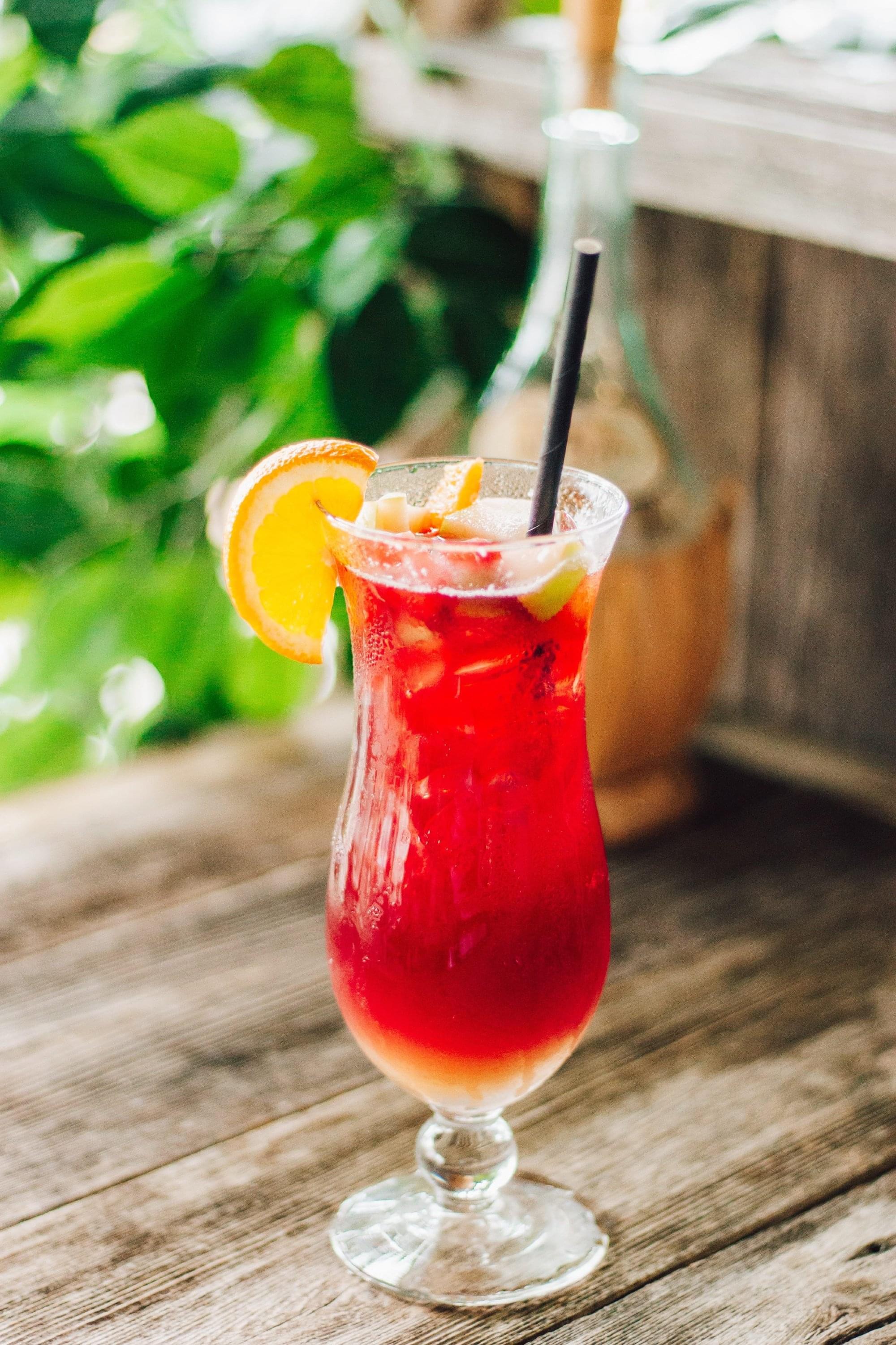 A red tropical drink in a daiquiri glass with fruit on top