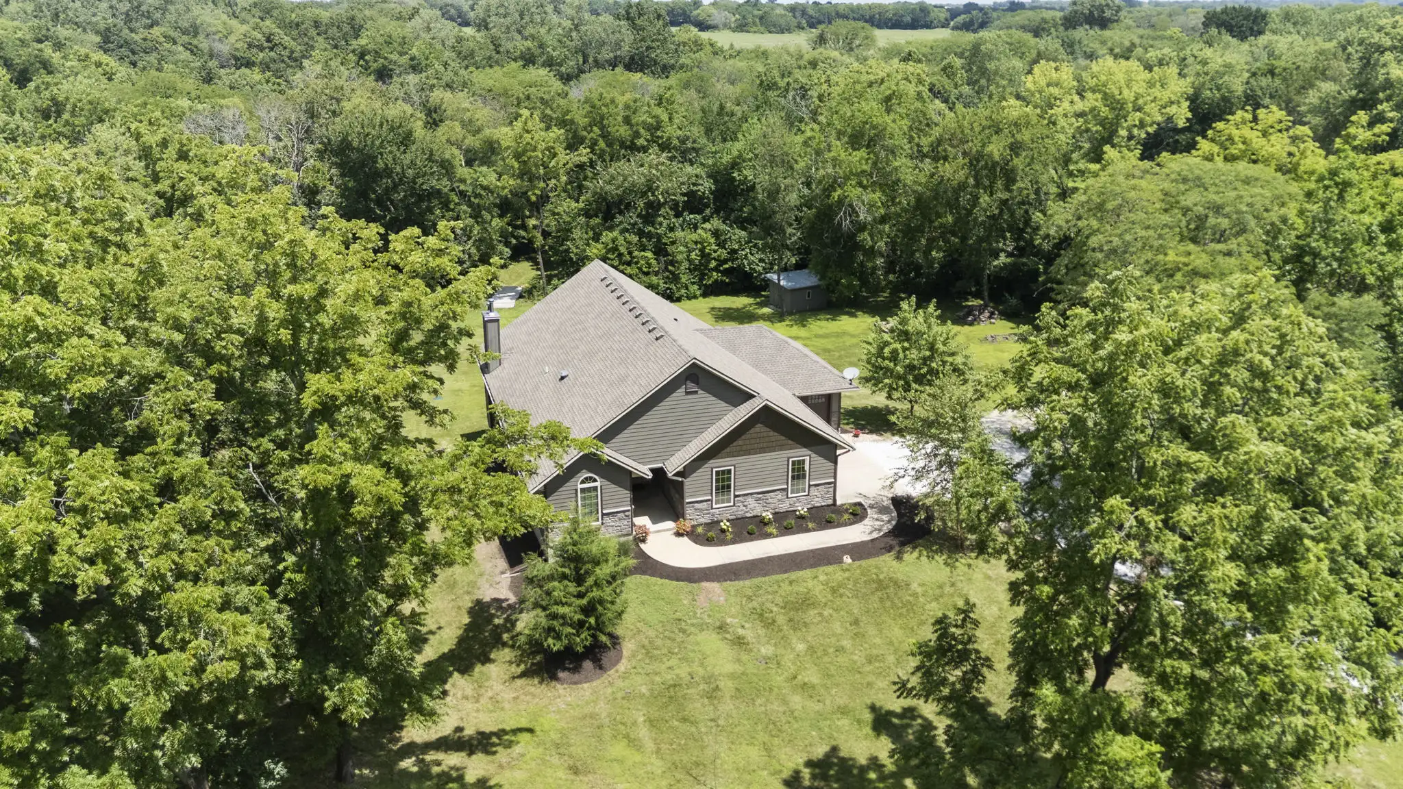 Aerial view of a reverse 1.5-story home surrounded by mature trees on 4.9 wooded acres at 1404 E 183rd St, Belton, MO