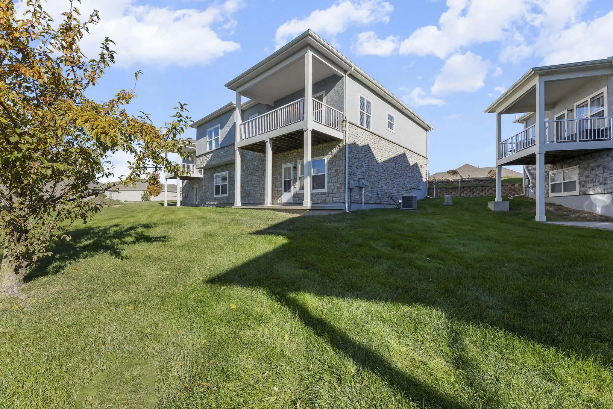 Backyard of 21962 W 116th Terrace Olathe KS 66061 — walk-out ranch with covered deck, stone foundation, and green lawn on a sunny day.