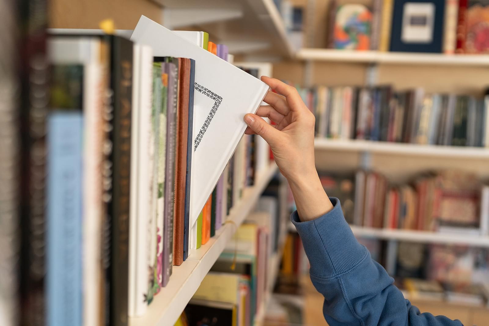 A hand pulling a book off of a shelf