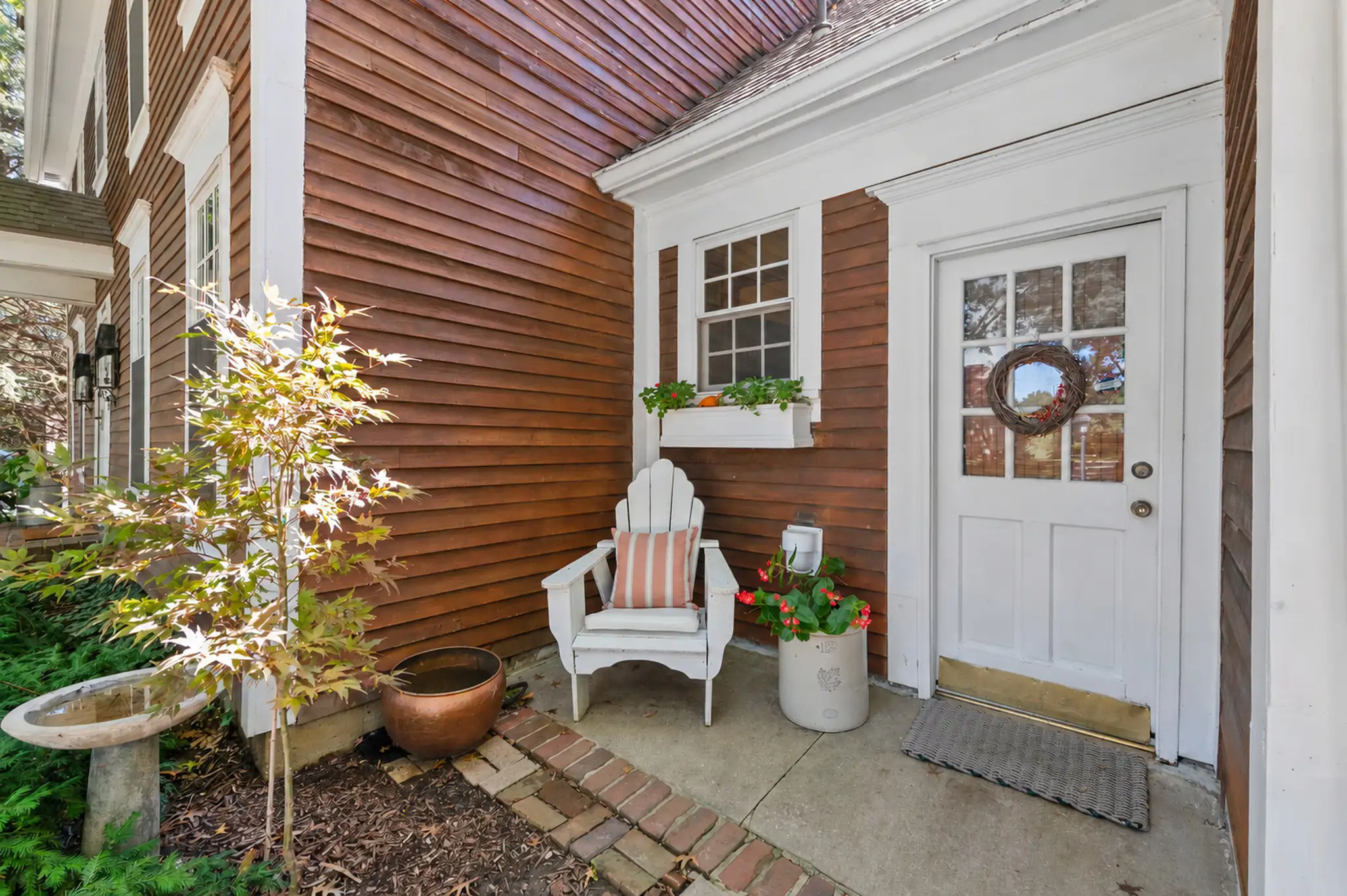 Covered side entry with white paneled door, window box and brick-edged walk