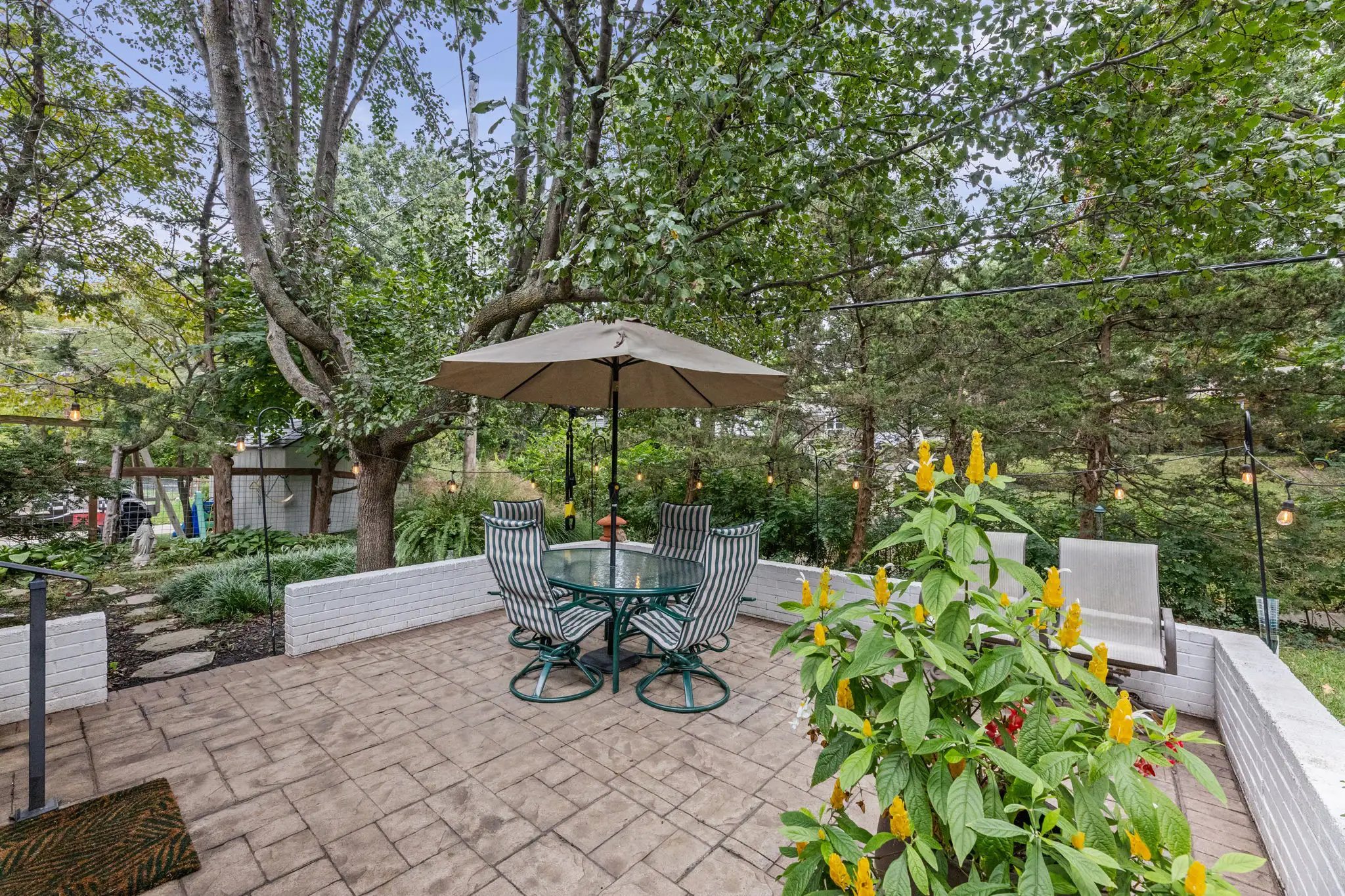 Paver patio with a low brick wall, string lights and flowering plants