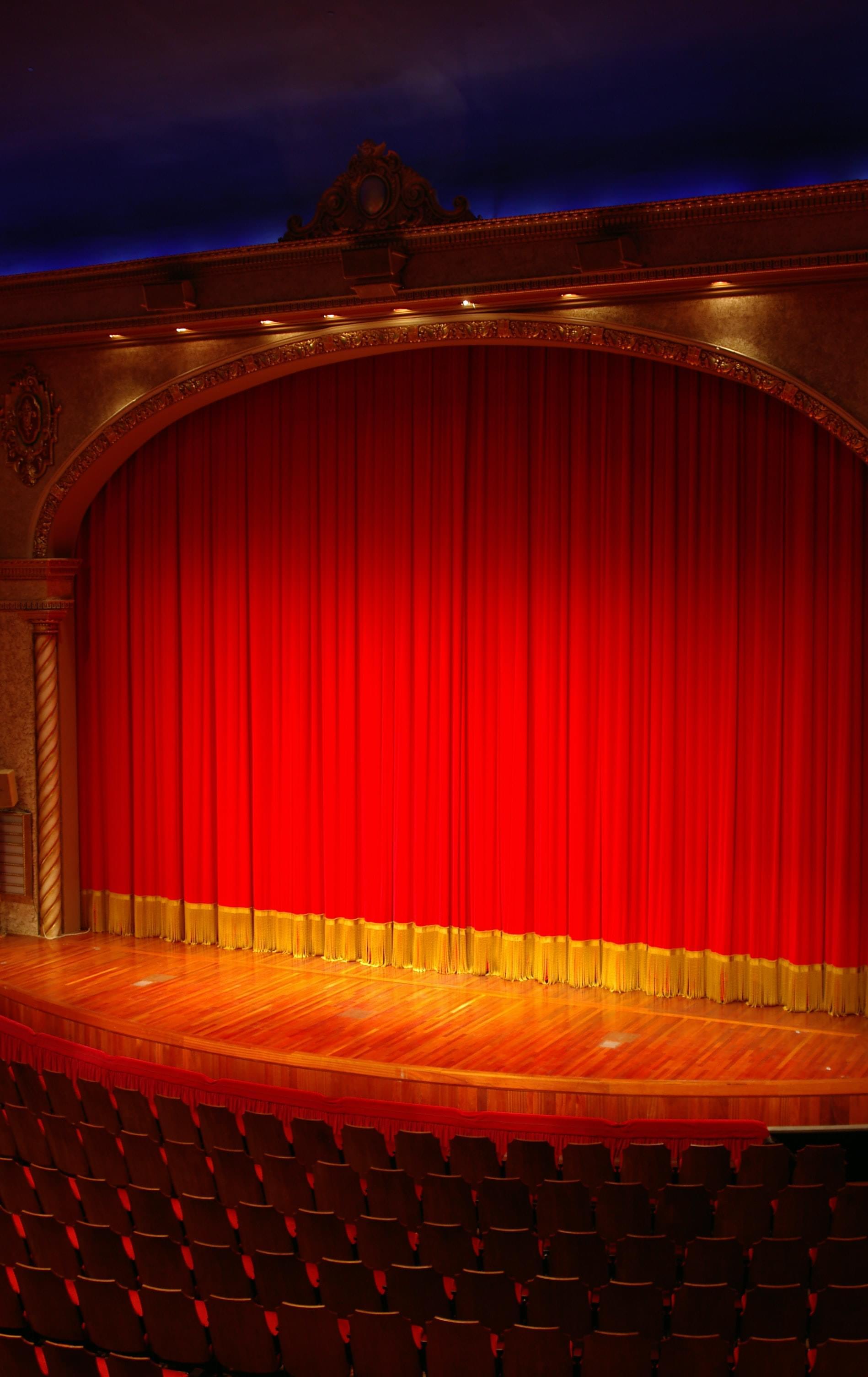 A classical stage with a closed red curtain and stage lights