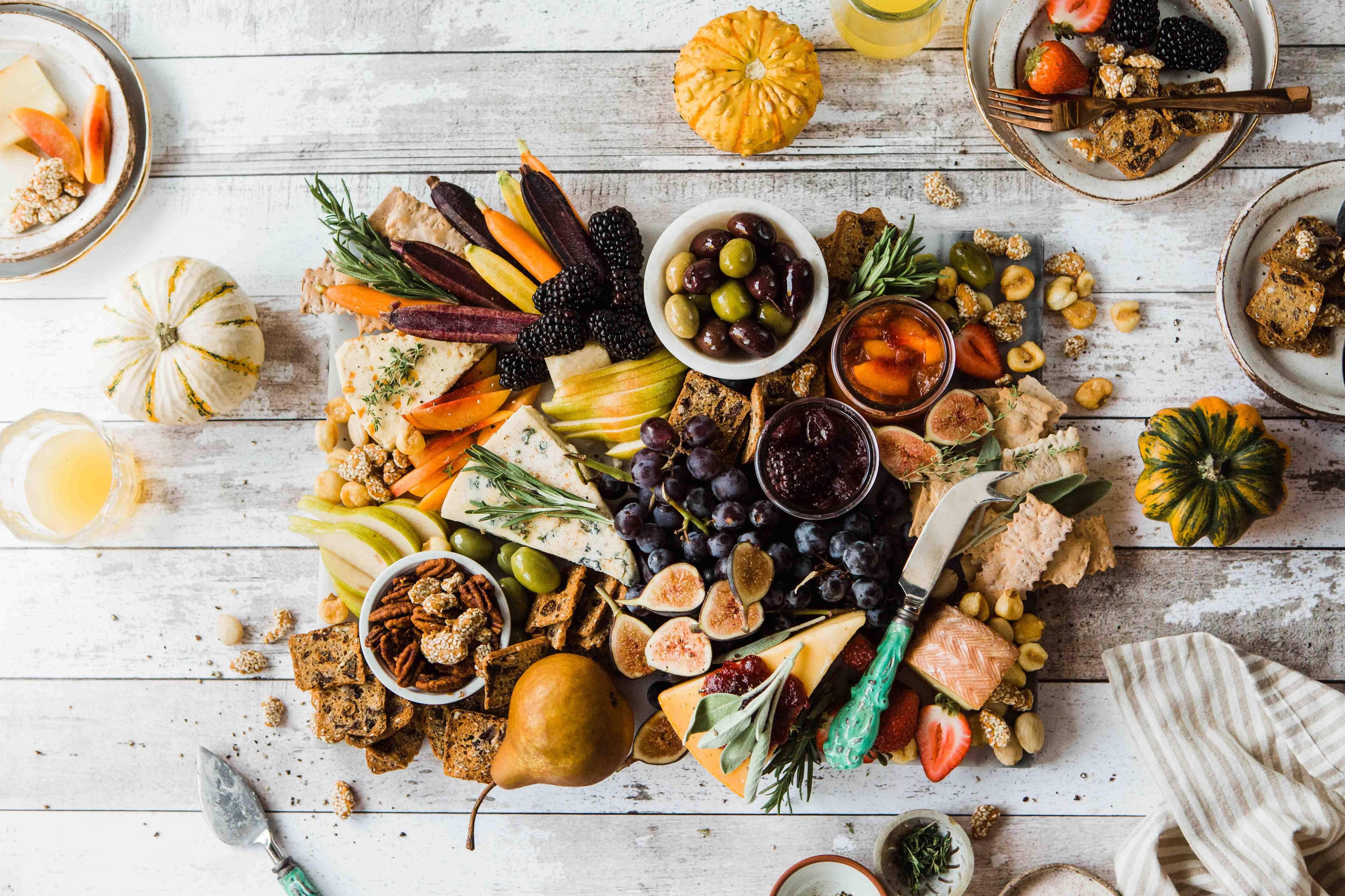 A fancy charcuterie board loaded with fruits, vegetables, cheeses, olives, crackers, sauces, and more