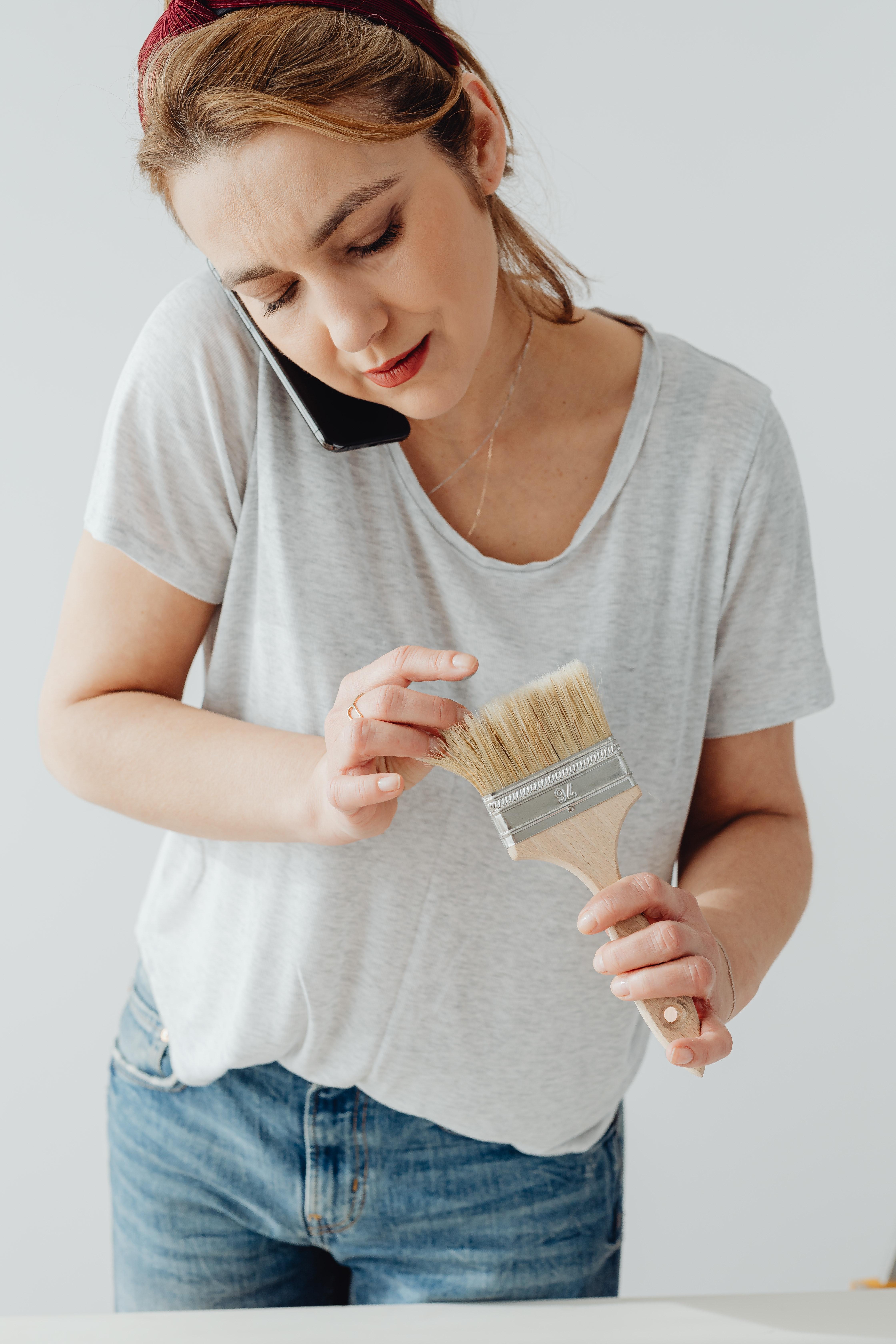 An auburn-haired woman talking on the phone while holding a paintbrush