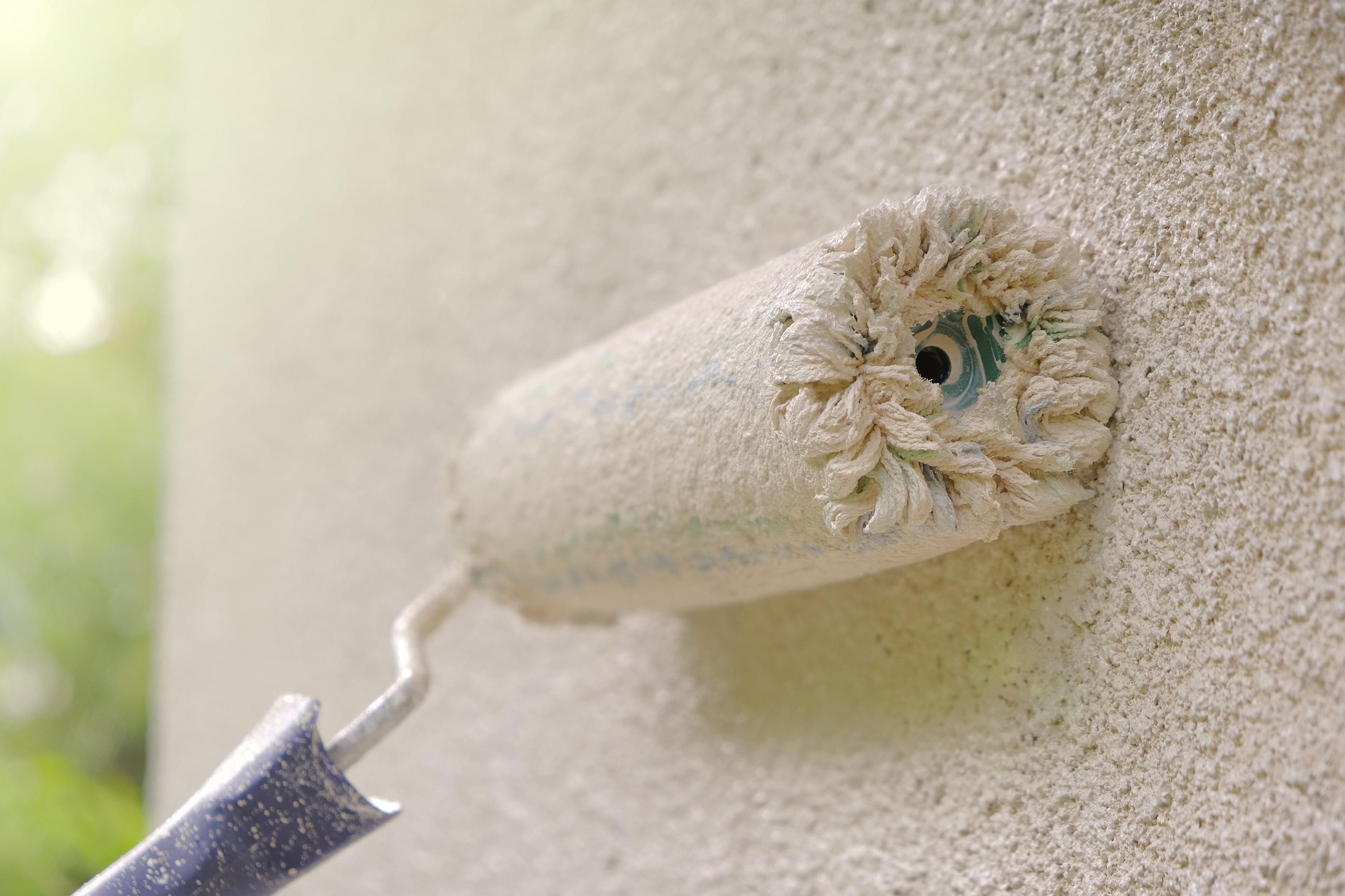 A roller painting a stucco wall beige