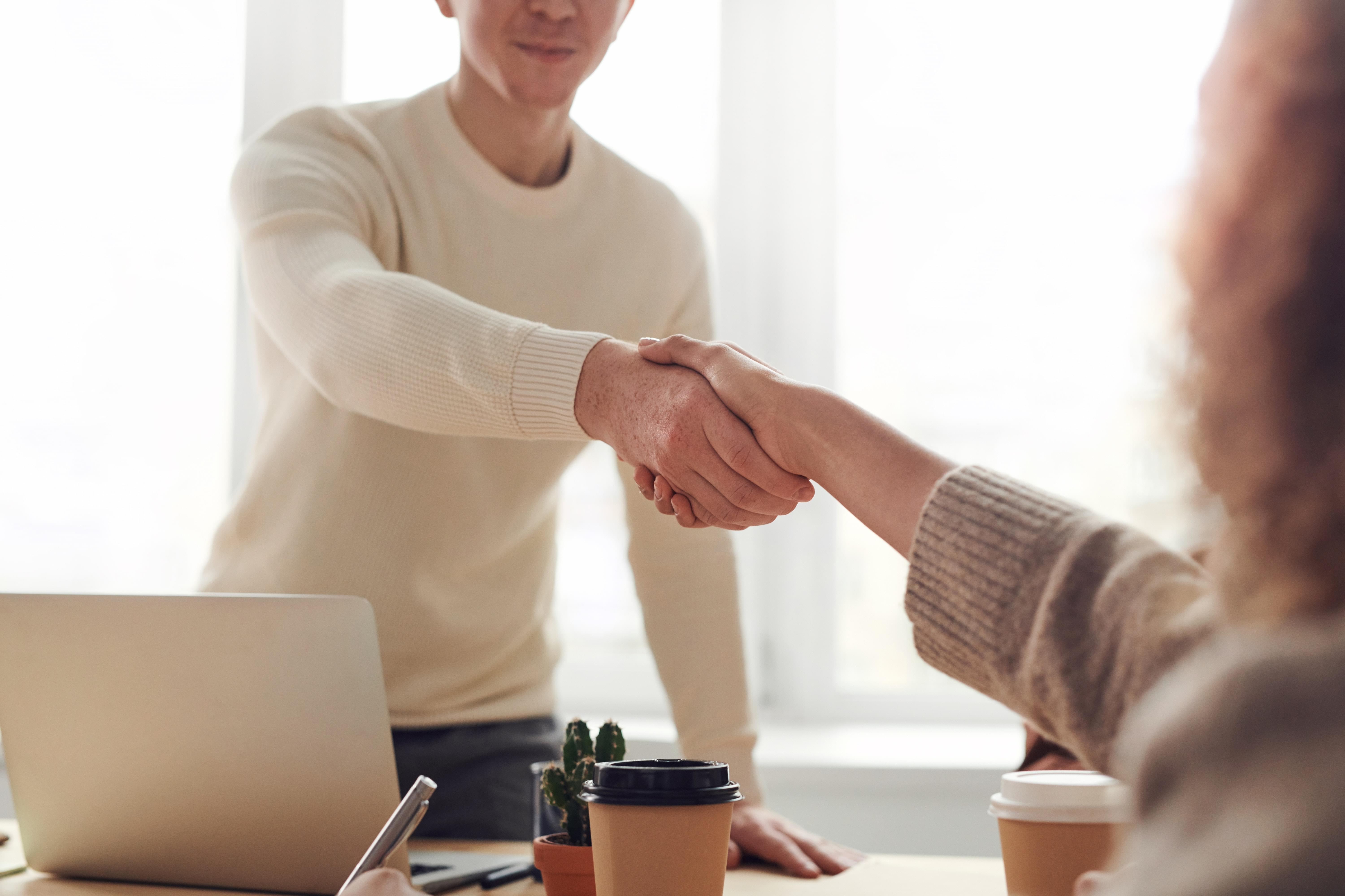 Two people shaking hands across a table after negotiation