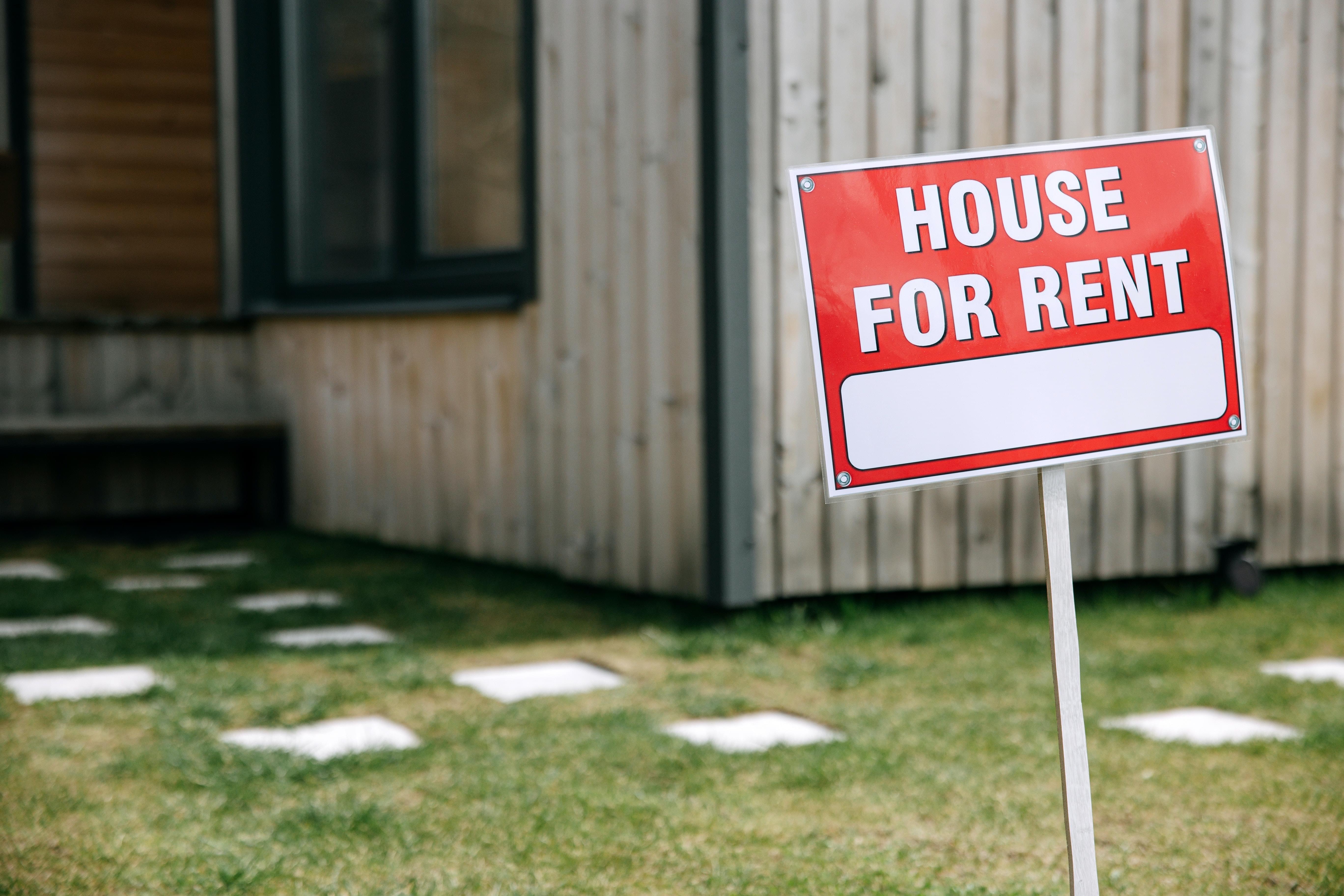 A red "house for rent" sign planted in the grass in front of a home
