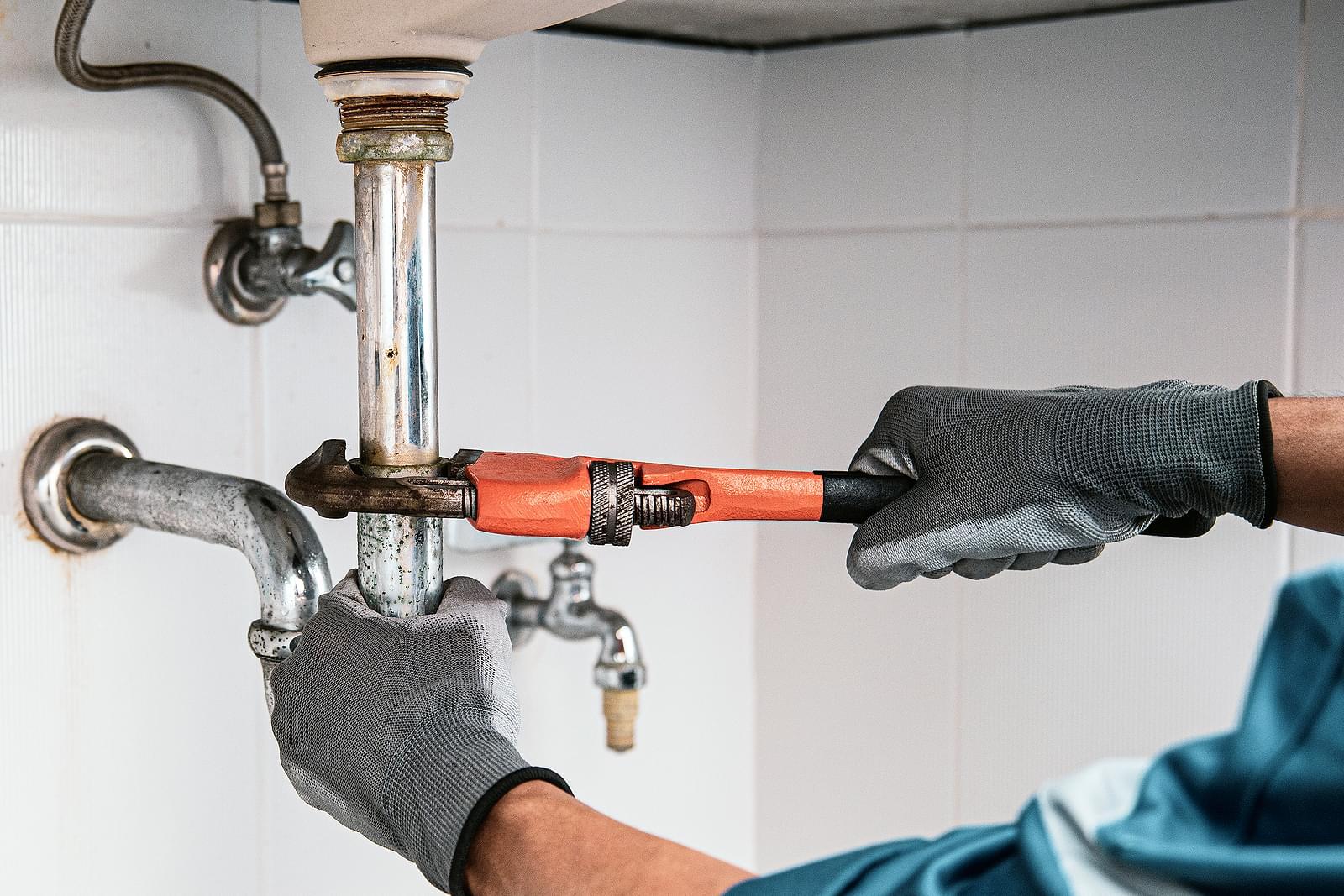 A pair of gloved hands repairing the plumbing under the sink