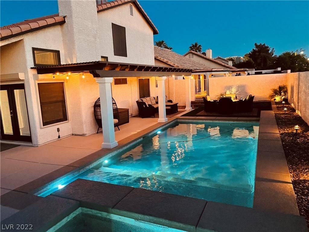 The gorgeous, well-lit outdooor space with a covered patio, outdoor seating, and a lit pool.