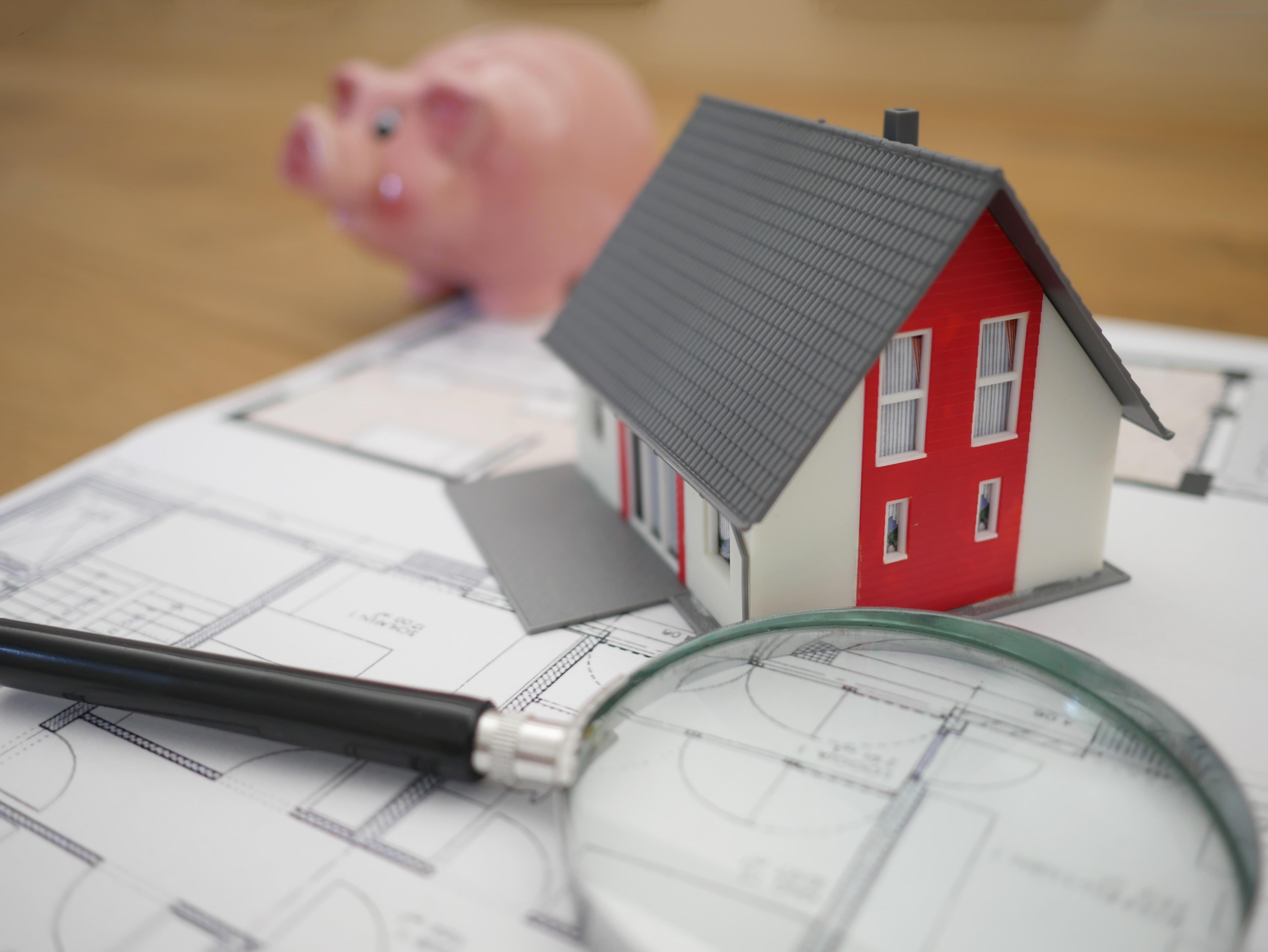 A home, magnifying glass, and piggybank on top of a house plan