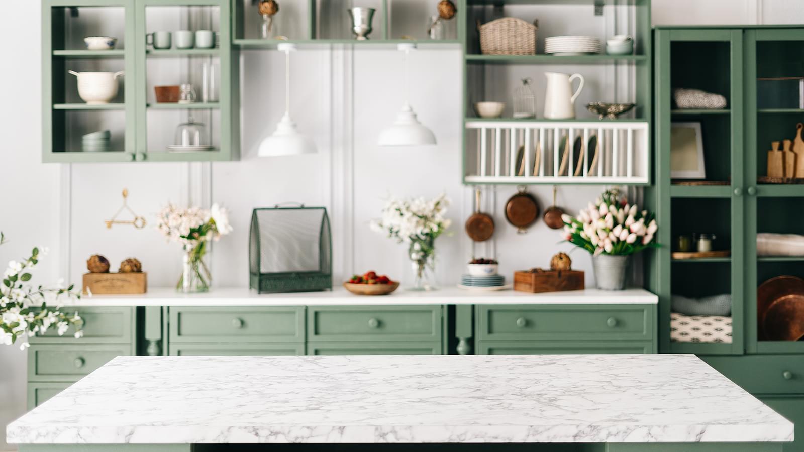 A kitchen with quartz countertops, green cabinets, fresh flowers, and other accessories