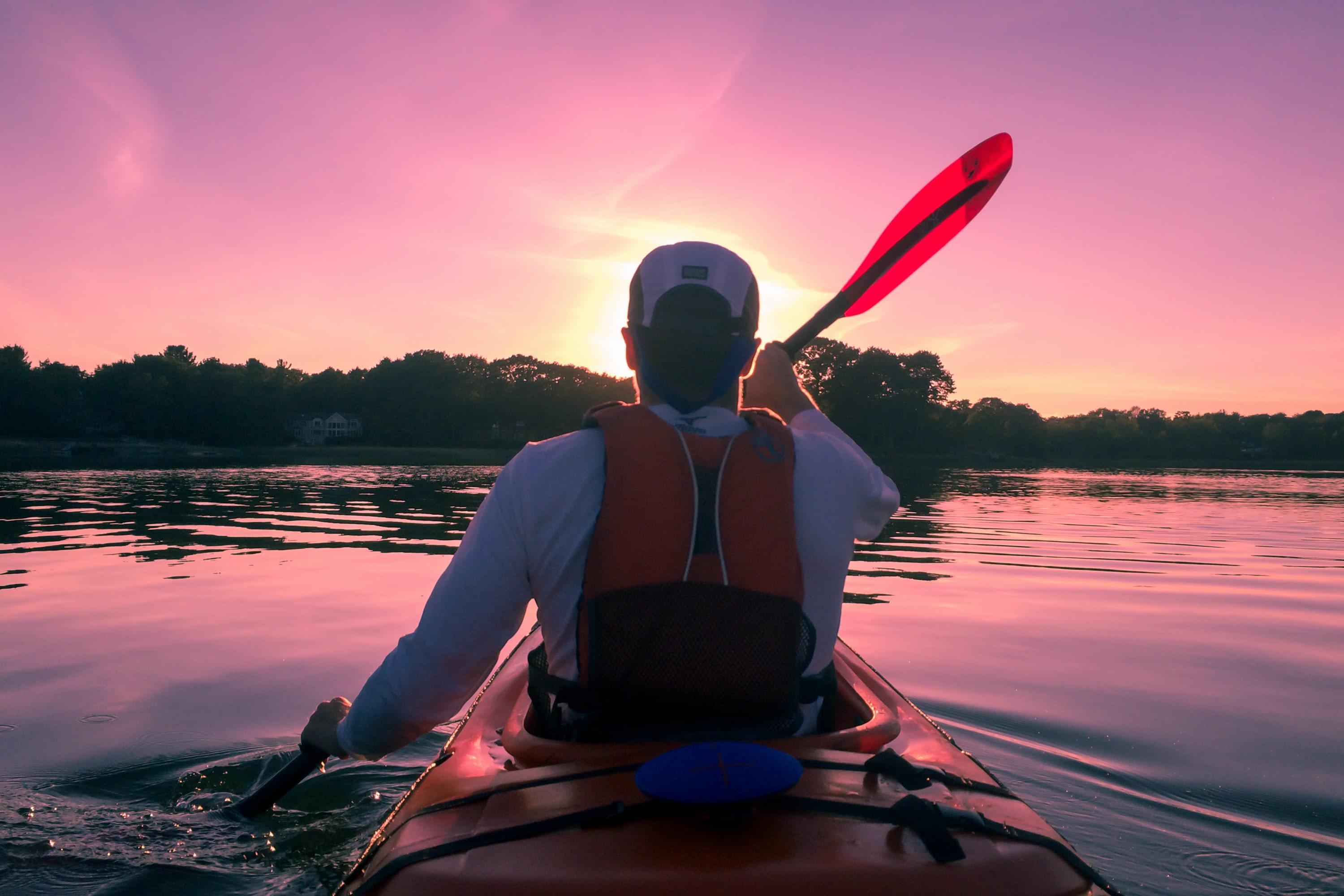 A person paddling a kayak on calm waters at sunset