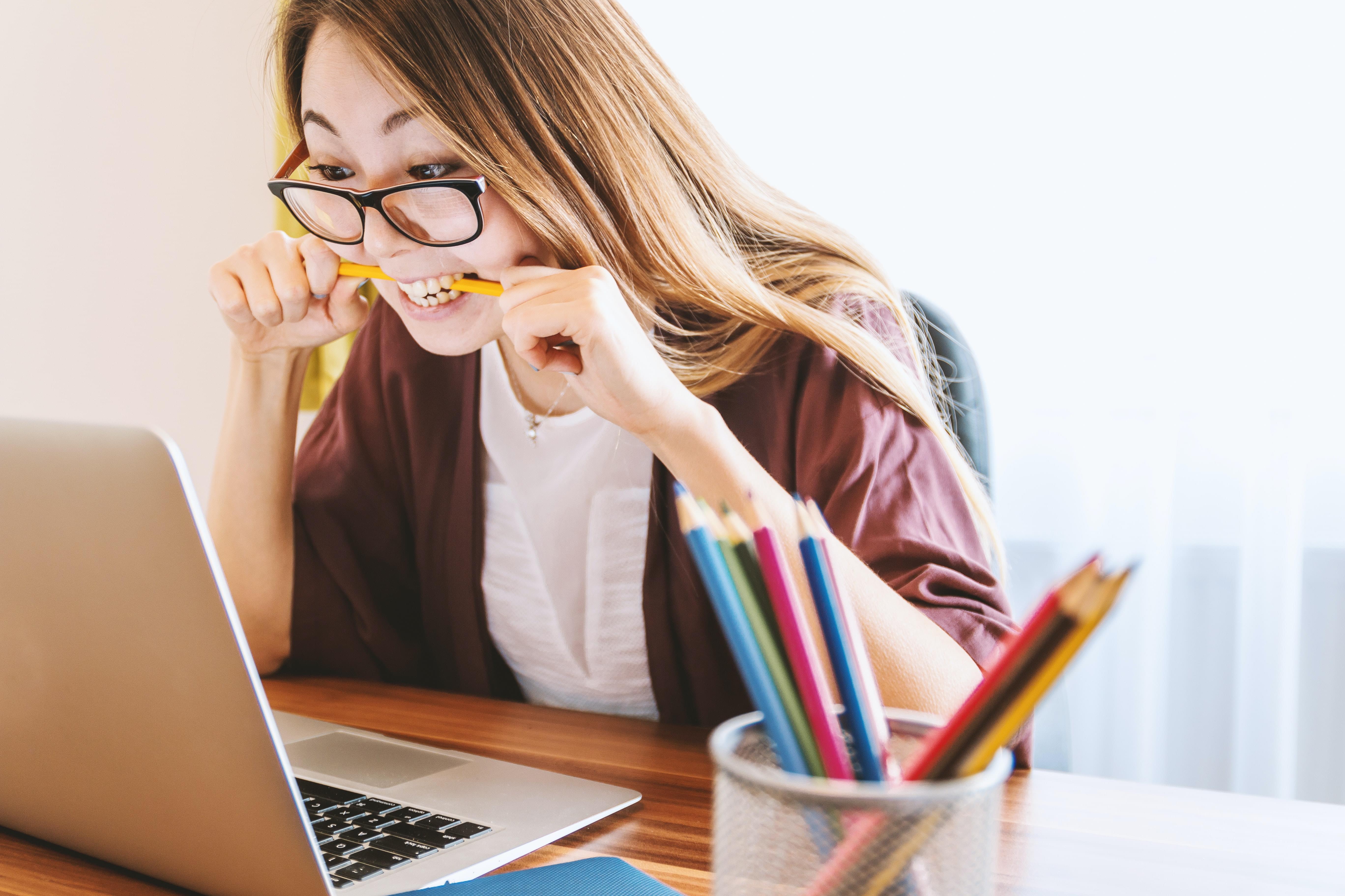 A stressed-out woman biting a pencil while looking at her computer screen