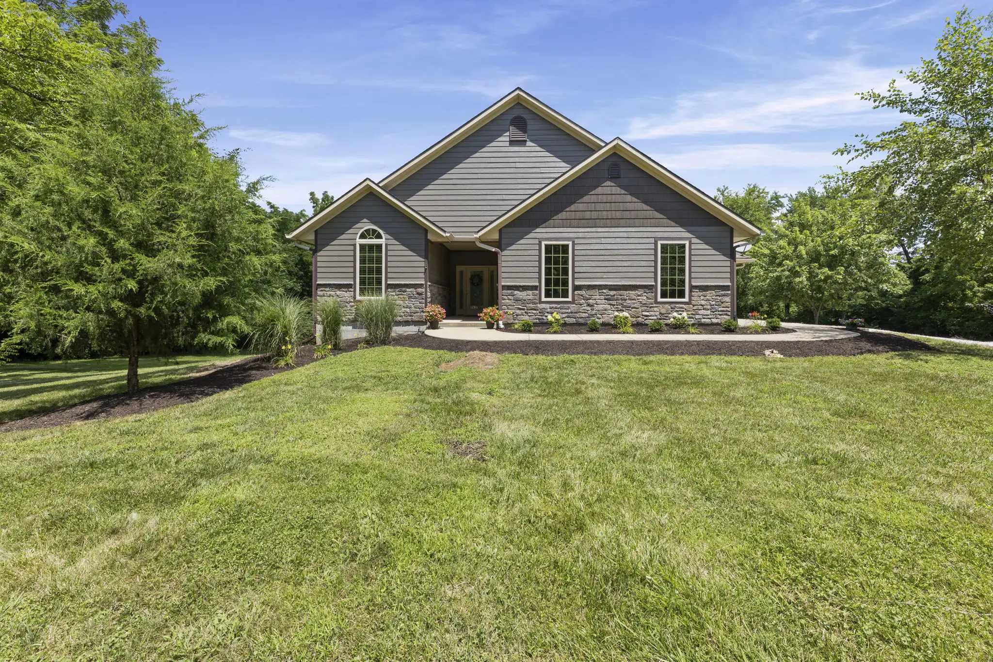 Craftsman-style reverse 1.5-story home with stone accents and mature trees.