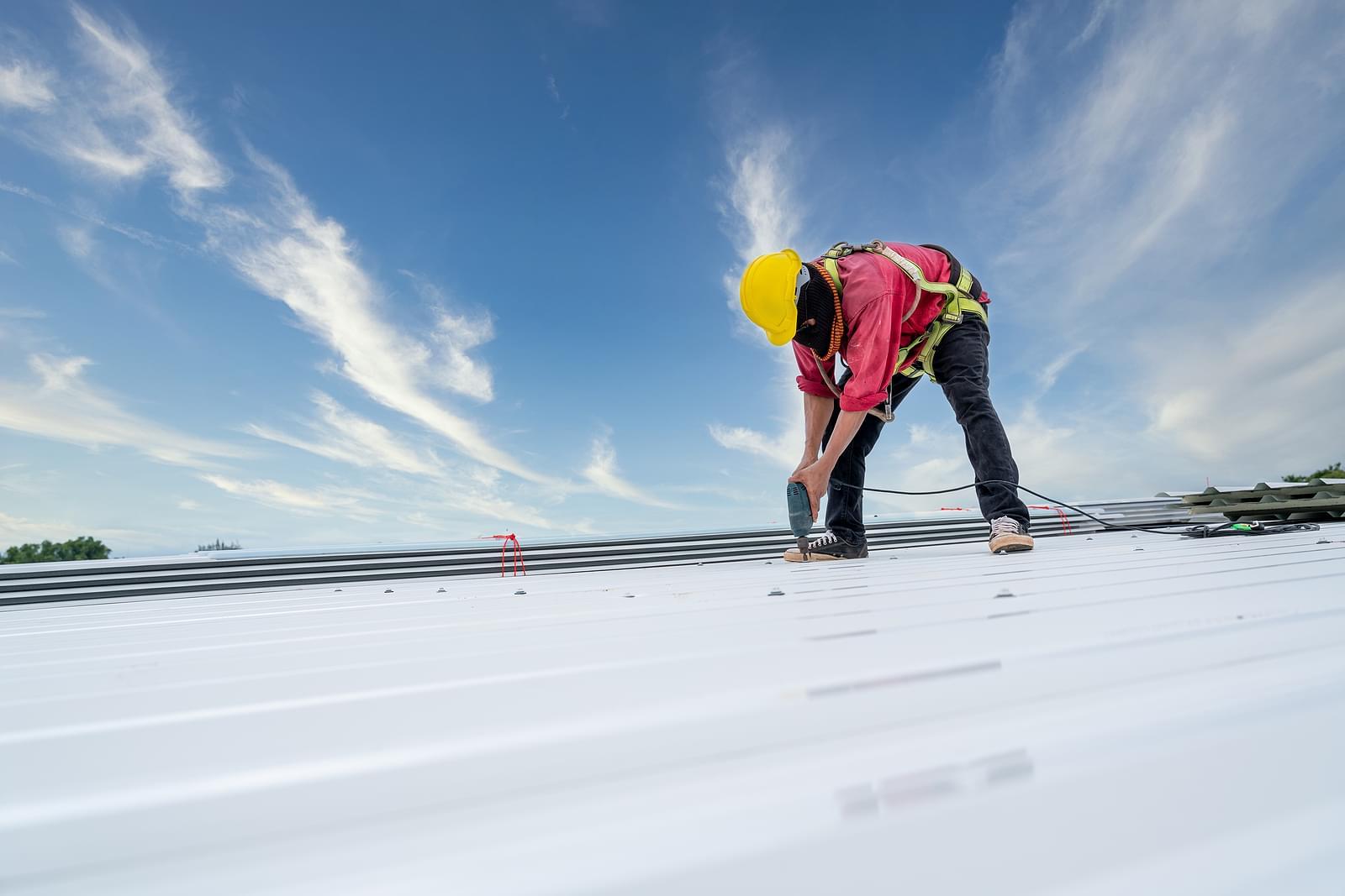 A construction worker installing white roofing material in front of a blue sky