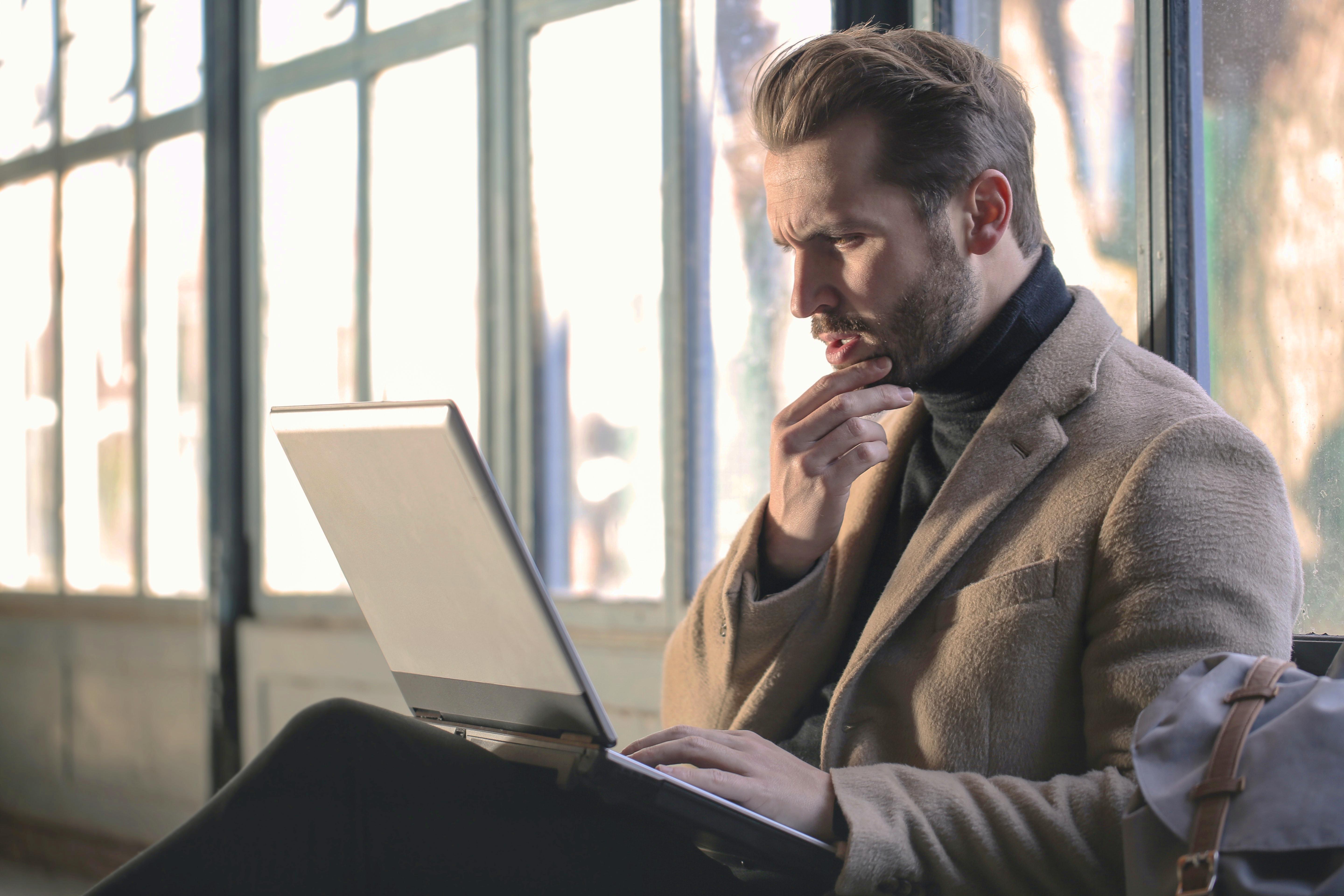 A man holding his chin with a furrowed brow as he analyzes what's on his computer screen