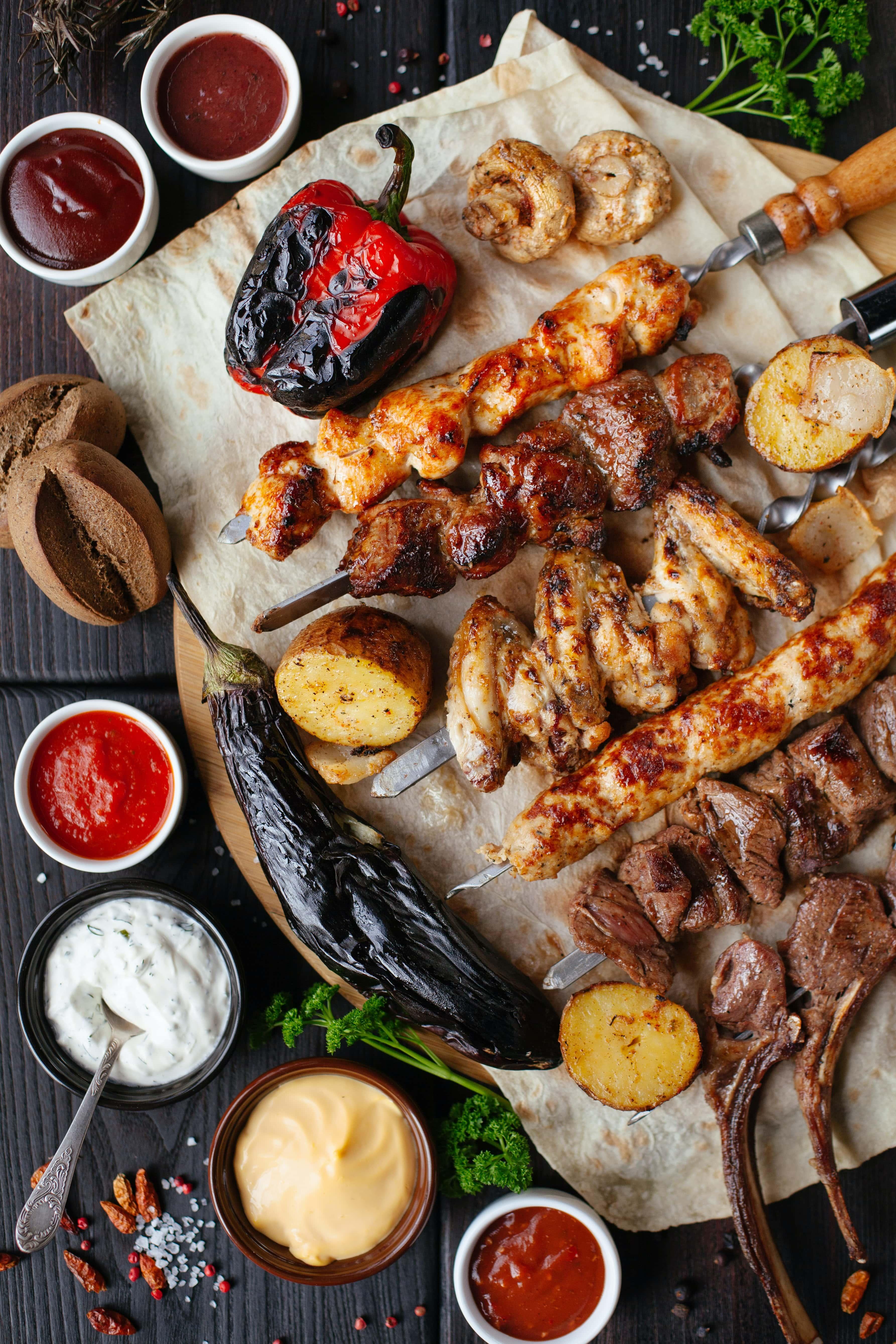 Kabobs of grilled meat surrounded by grilled vegetebles, mushrooms, and sauces