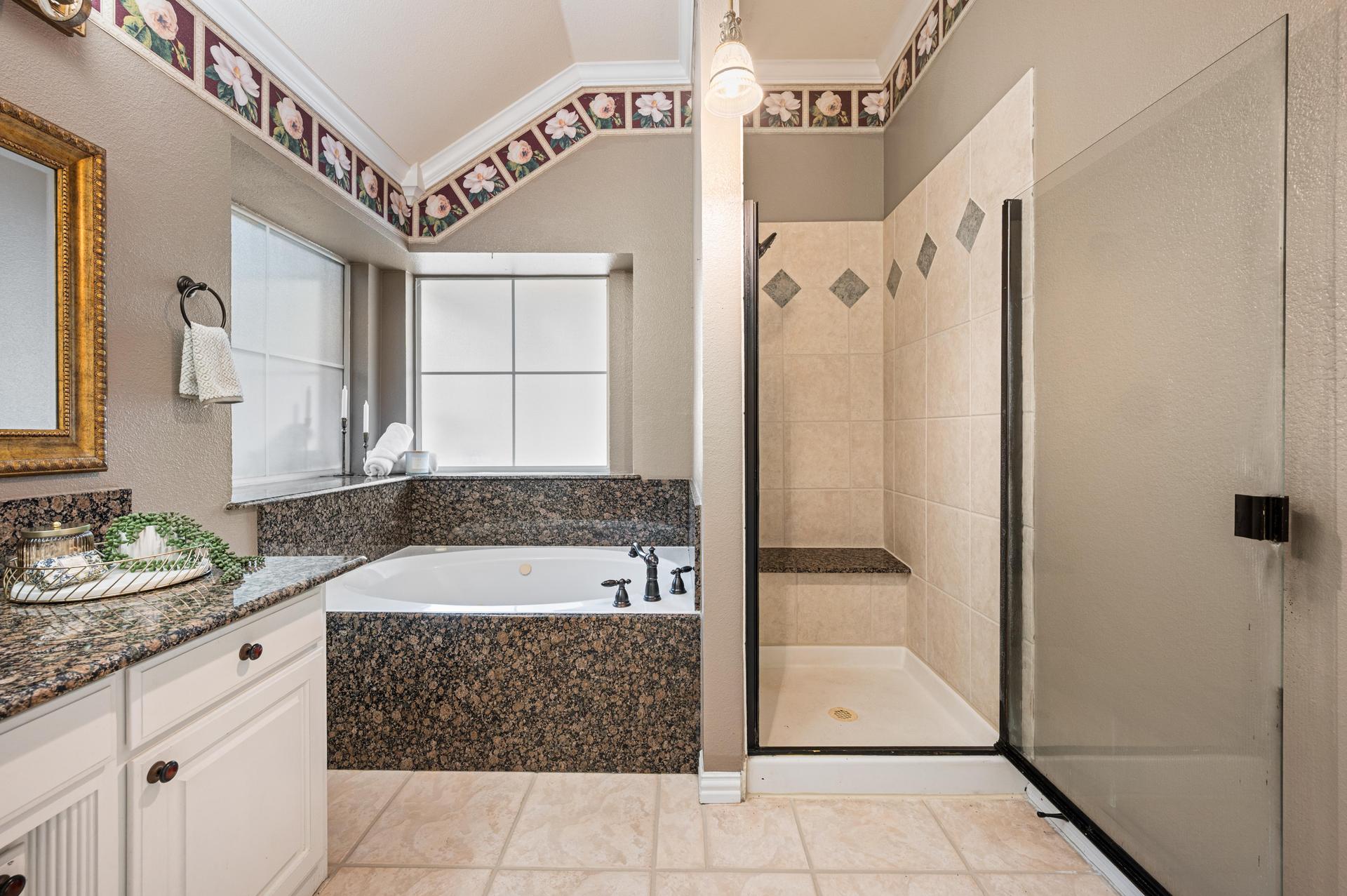 Primary bathroom with jetted soaking tub, separate glass shower, granite countertops, and tile flooring