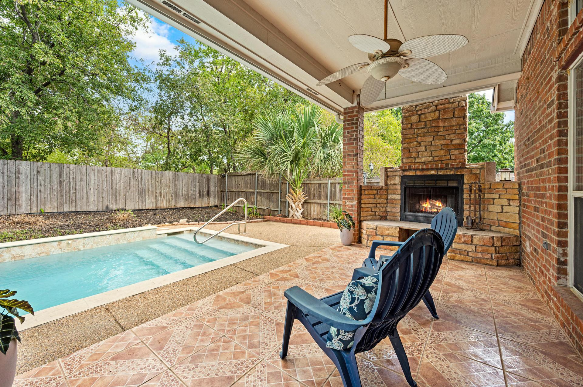 Covered outdoor patio with ceiling fan, outdoor fireplace, tile flooring, and views of the pool