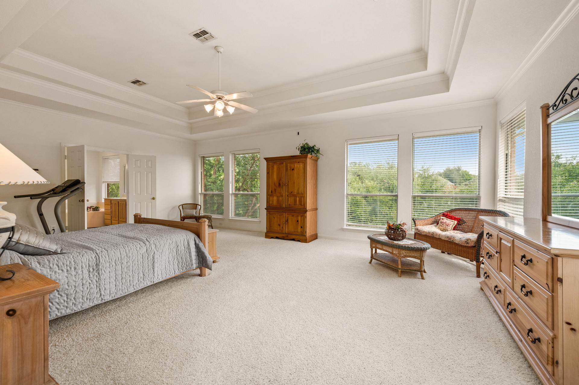 Spacious primary bedroom with tray ceiling, sitting area, and large windows at 7626 Lakecrest Circle