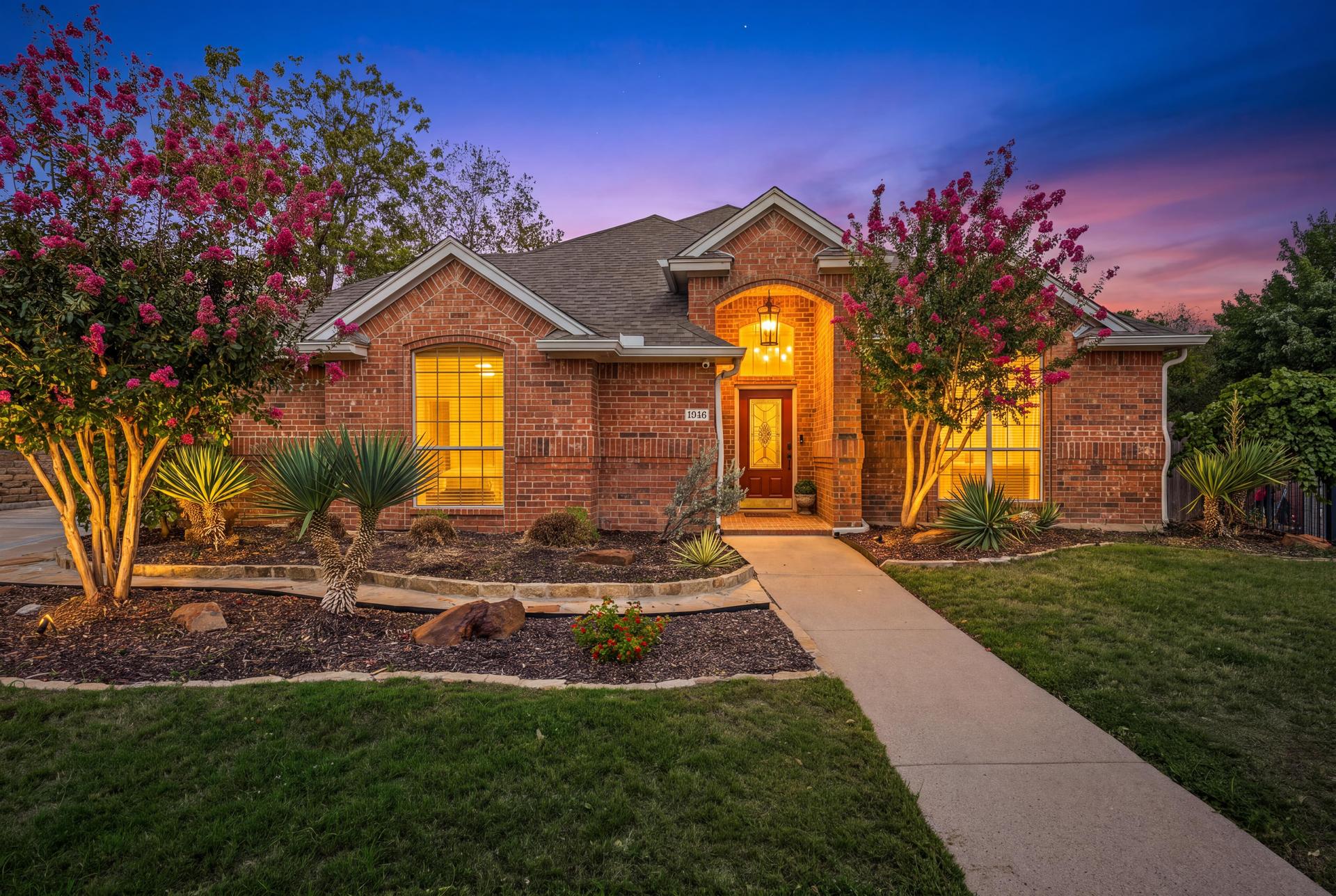 Front exterior of the red-brick home with covered entry and landscaped front yard