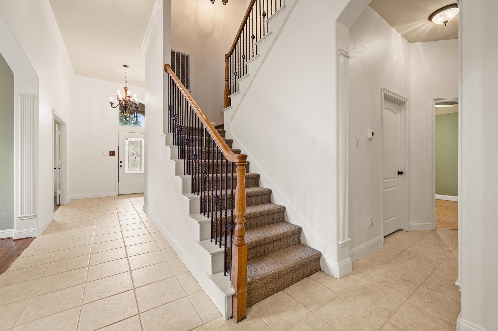 Entry hallway with tiled flooring, decorative trim, and staircase with wood handrail and dark metal balusters