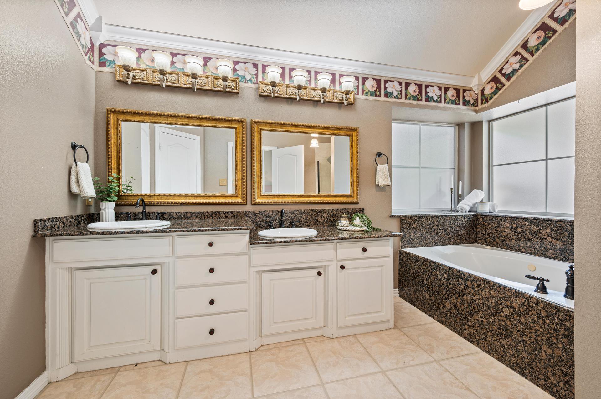 Primary bathroom with dual vanities, granite countertops, jetted soaking tub, and separate glass shower