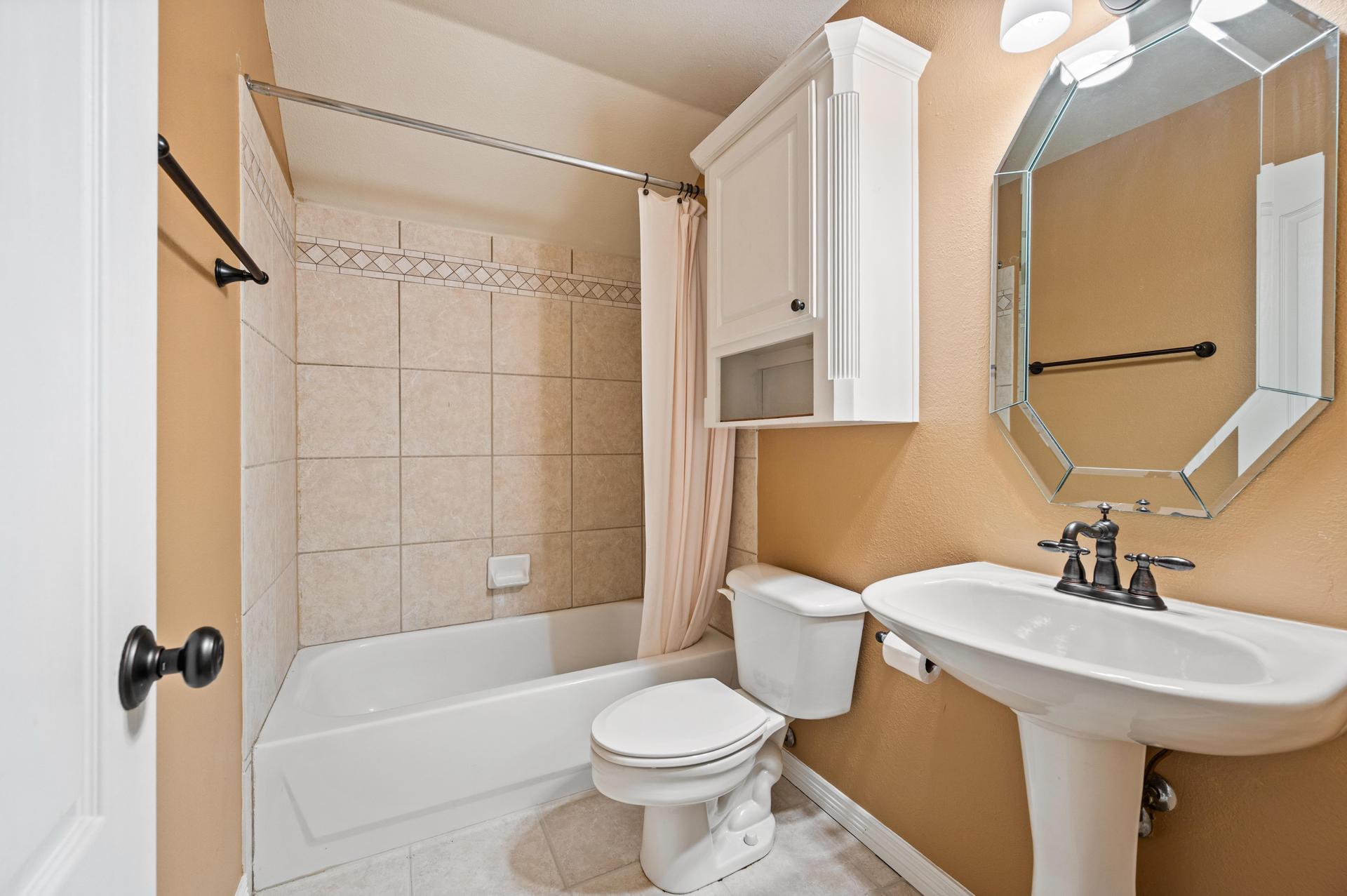 Full bathroom with bathtub, tiled shower surround, pedestal sink, toilet, and mirrored medicine cabinet