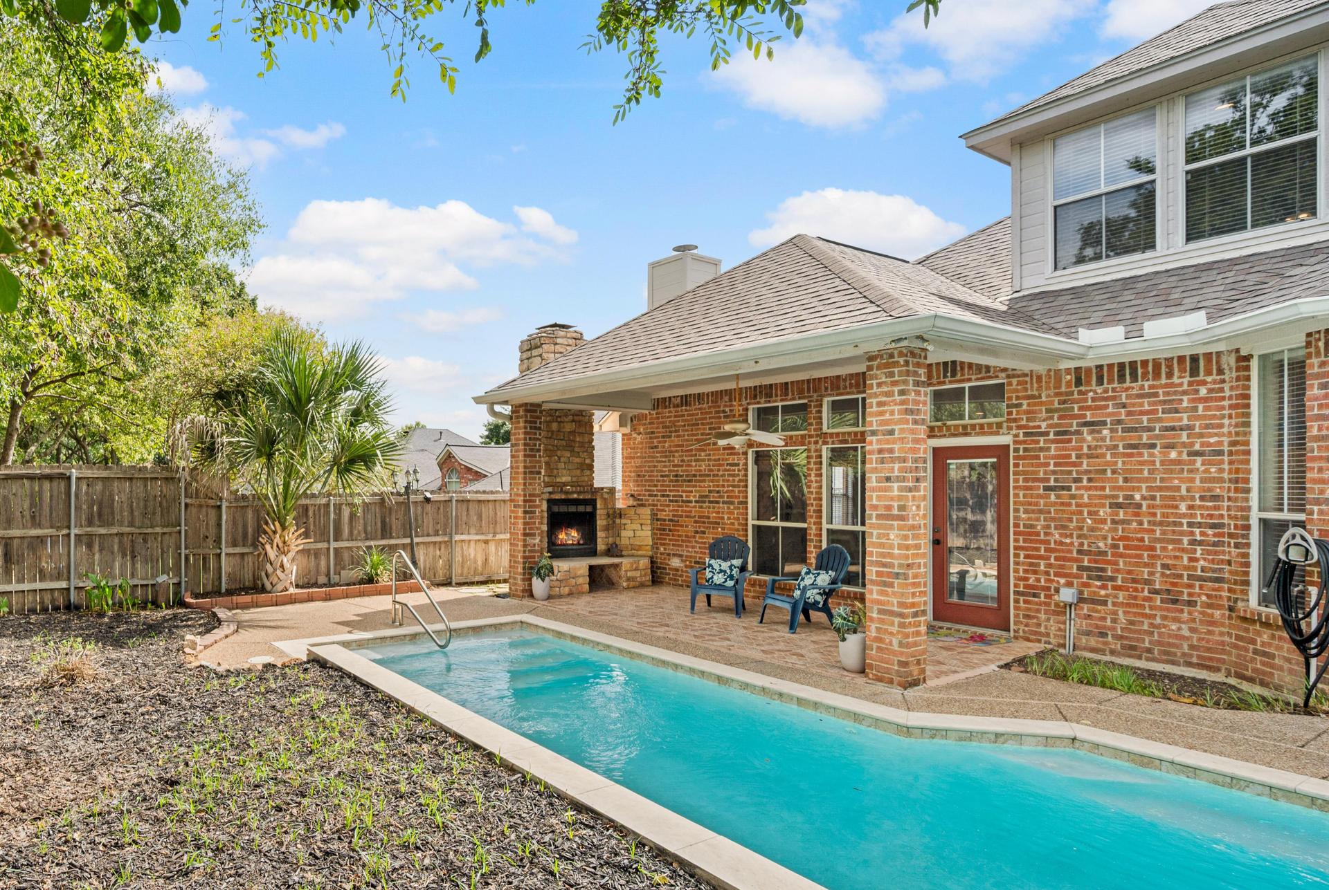 Swimming pool beside the brick home with a covered patio and privacy fence