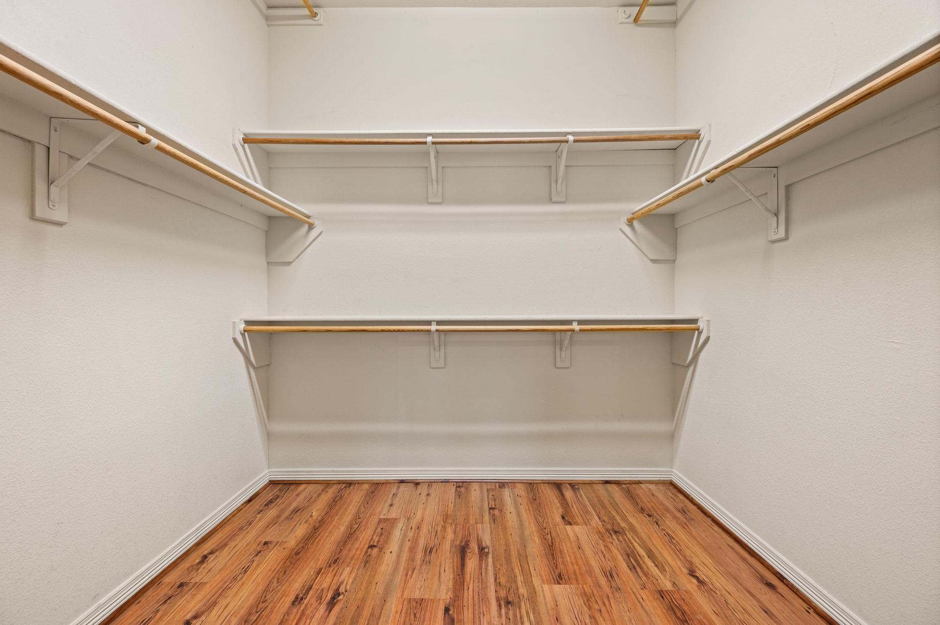 Walk-in closet with wood-look flooring, multiple hanging rods, and storage shelves along three walls