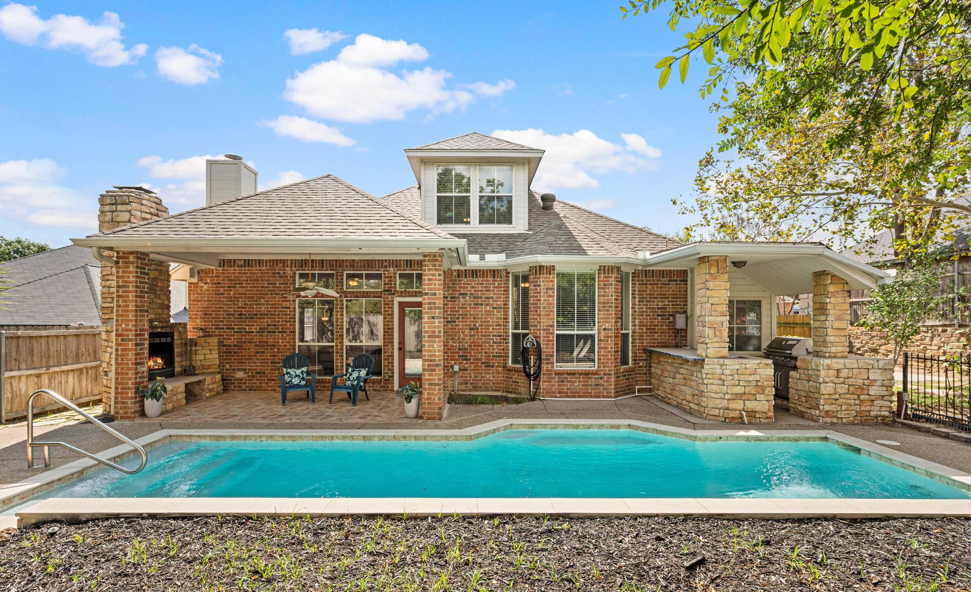 Wide backyard view with swimming pool, covered patio, landscaped areas, and detached structure