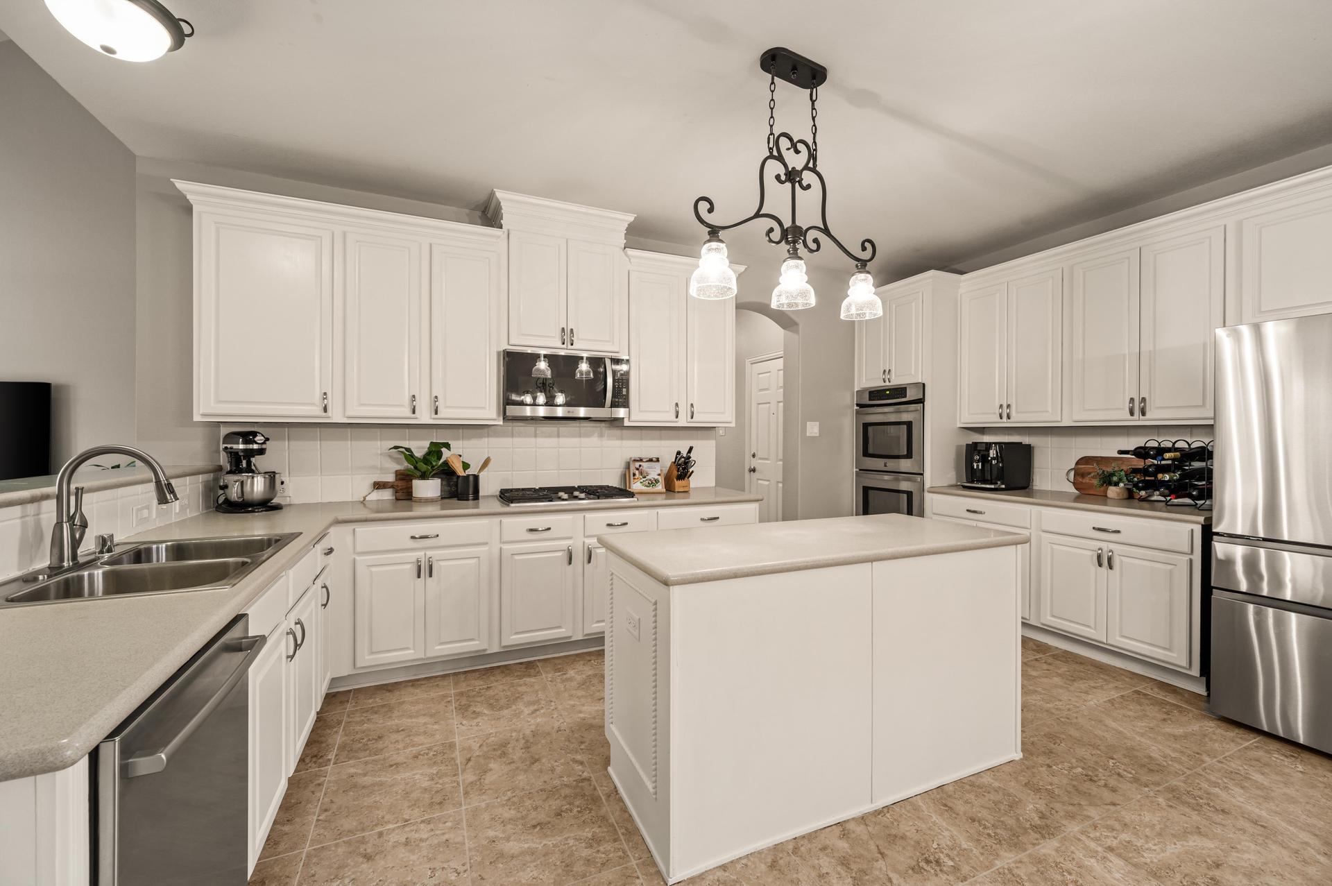 Bright open-concept kitchen with a large center island, white cabinetry, stainless steel appliances, double ovens, and generous prep space at 1404 Big Falls Drive in Flower Mound, Texas.